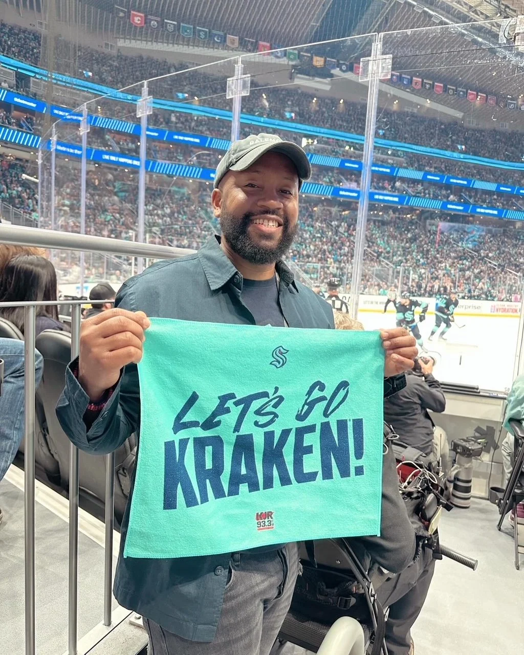 A person holding a "LET'S GO KRAKEN!" towel at a hockey game with a crowded arena in the background.