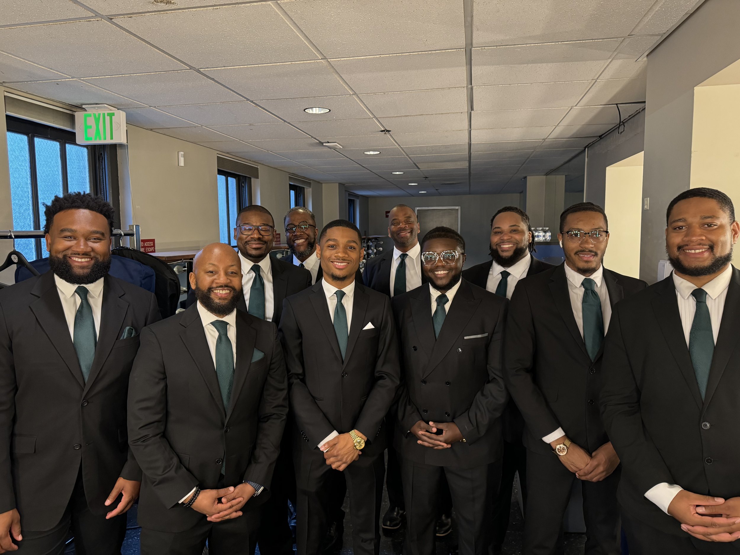Group of men in suits with teal ties, smiling, standing indoors.