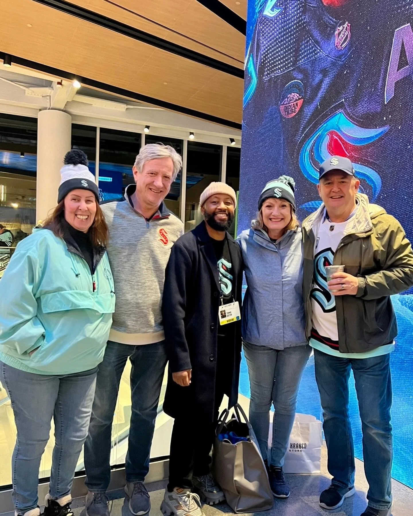 Group of five people standing indoors wearing Seattle Kraken apparel and smiling at a sports venue.