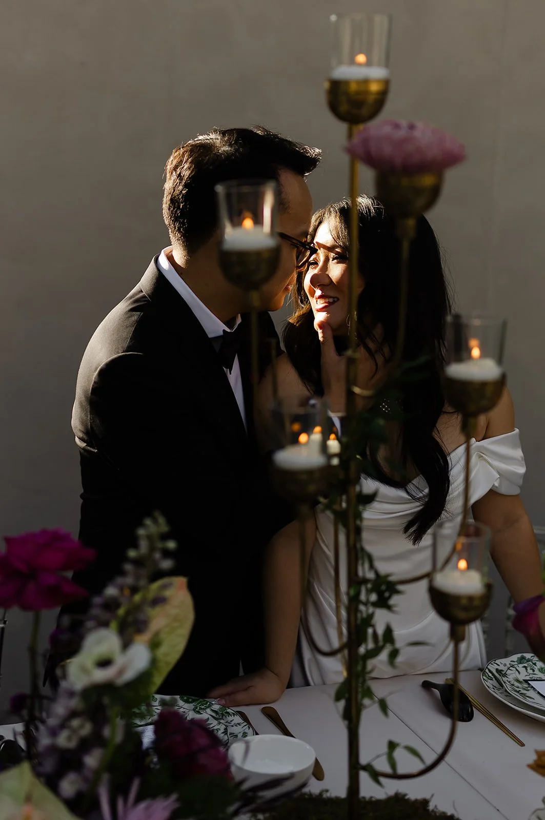 A couple dressed in formal attire at a romantic dinner, with candlelit decorations and flowers on the table.
