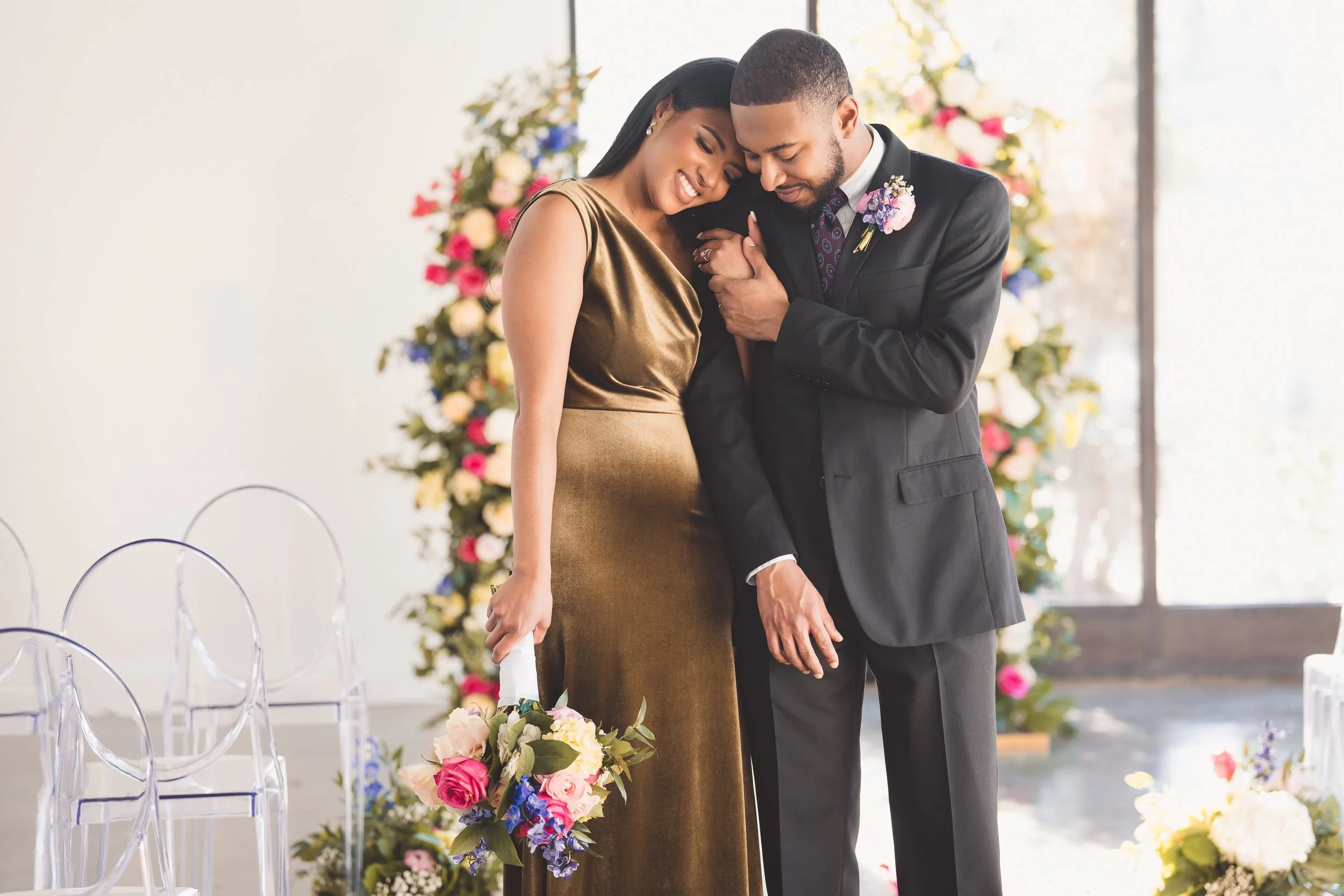 A couple on their wedding day, embracing and smiling with wedding flowers in the background.