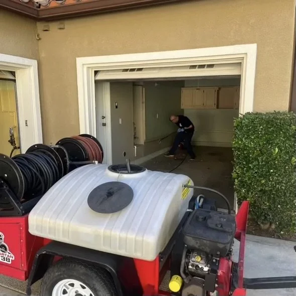 A worker cleaning or inspecting a garage floor with a power hose.