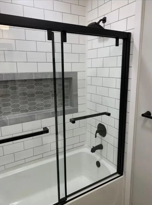 Bathroom shower with a black-framed glass door, white subway tile walls, gray hexagonal tile accent niche, and black fixtures.