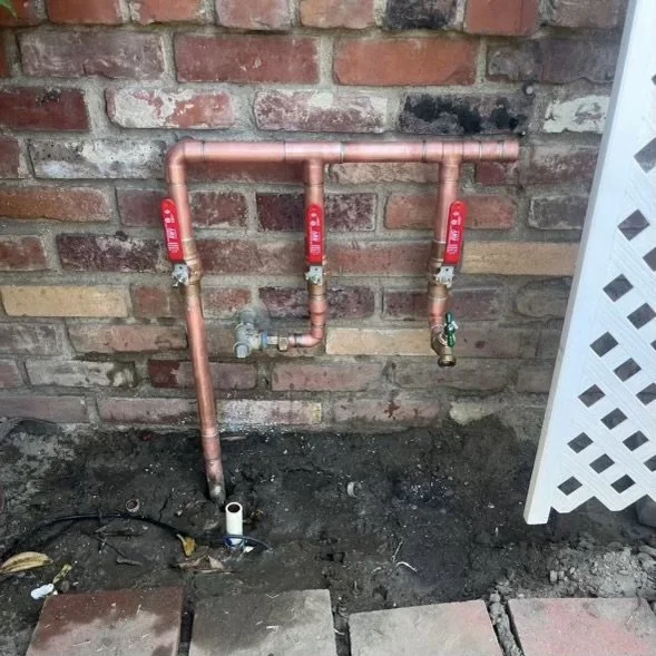 Copper water pipes and valves installed against a brick wall, with pipes extending into the ground.