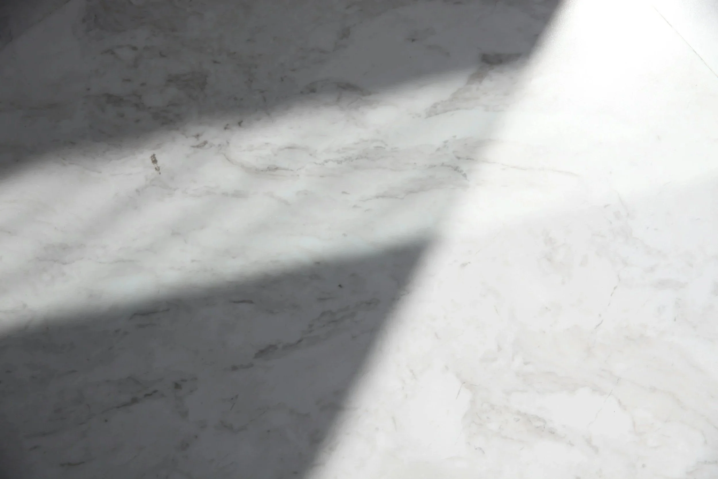 Close-up of a white marble surface with light and dark gray veining, partially covered by shadows.