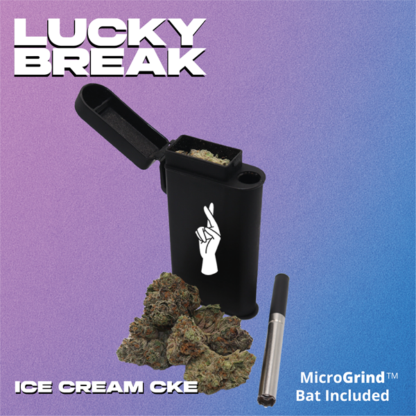 A black portable vaporizer device with a lid open, containing cannabis. Next to it are cannabis buds and a silver micro grind bat. The background is a gradient of purple and blue. Text reads 'Lucky Break,' 'Ice Cream CKE,' and 'MicroGrind Bat Included,' with an illustration of a hand making a peace sign.