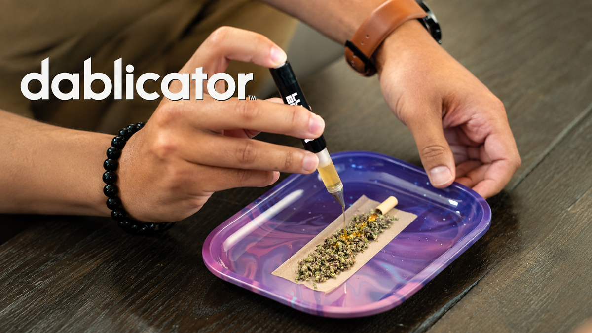 Person preparing a herbal blend with a syringe on a rolling paper on a purple tray, with a black beaded bracelet on their wrist and a brown watch, on a wooden table.