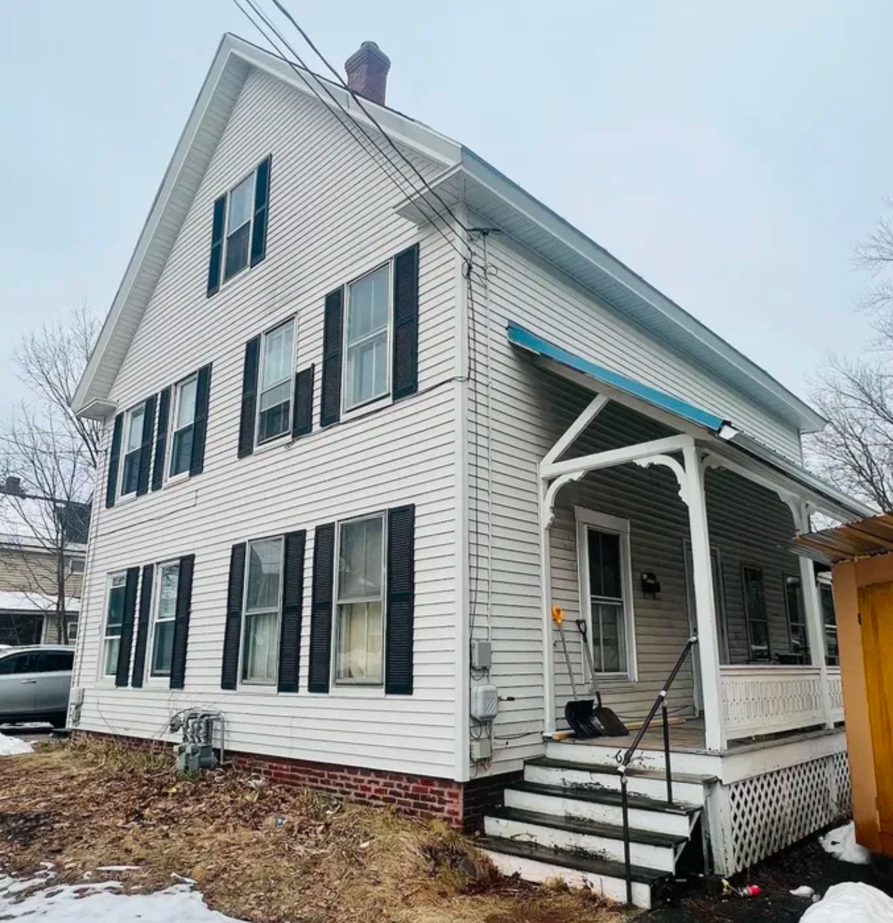 Two-story white house with black shutters, a small covered porch, steps, and minimal snow on the ground.