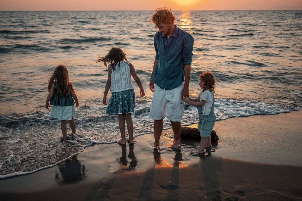 Ein Mann mit drei Kindern am Strand während des Sonnenuntergangs, sie stehen im Wasser und spielen.