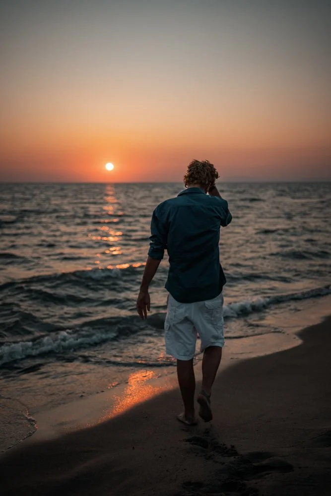 Mann läuft am Strand bei Sonnenuntergang ins Wasser.