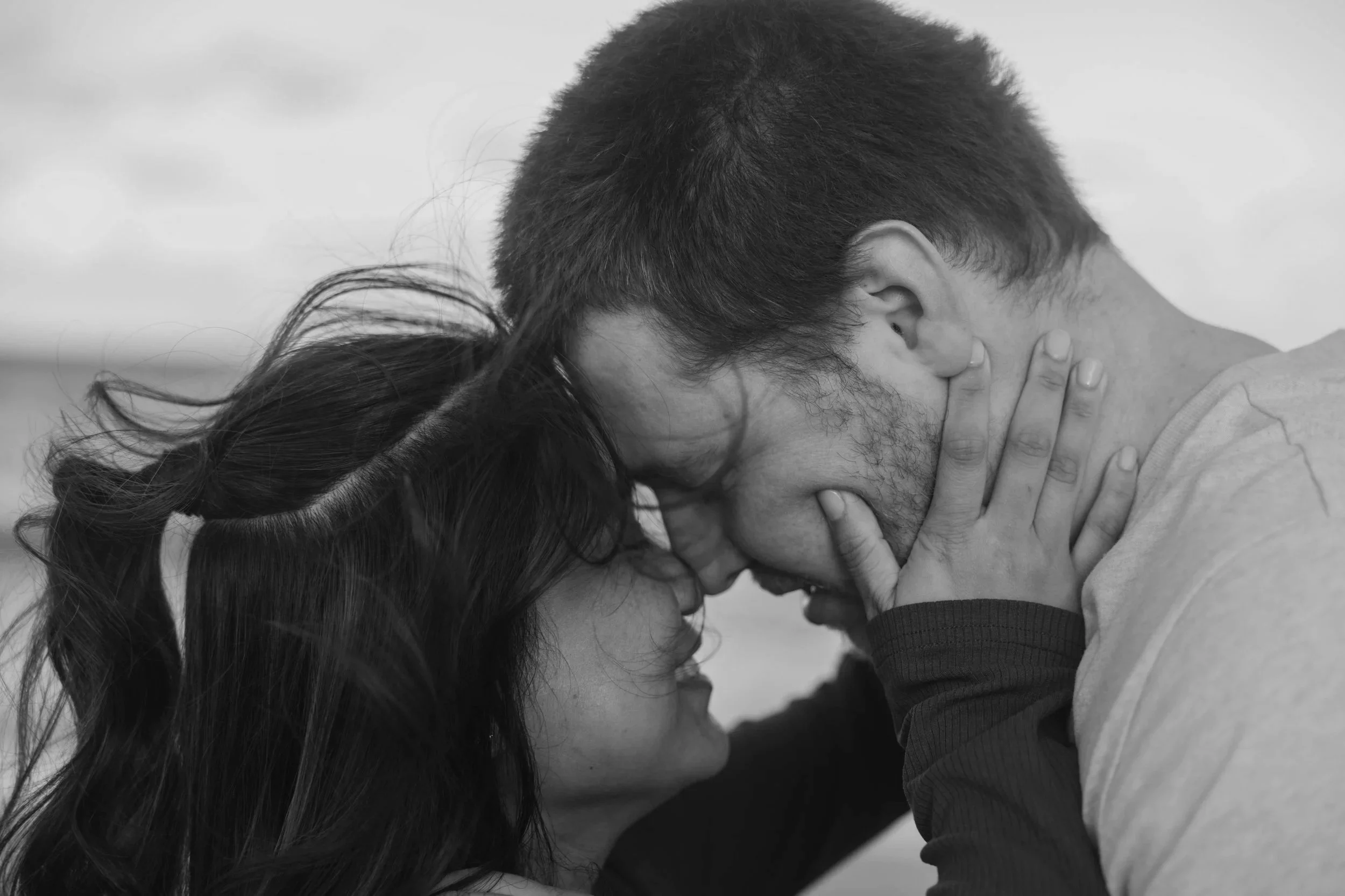 A black and white photo of a man and a woman touching foreheads with eyes closed, one woman's hand gently holding the man's chin.