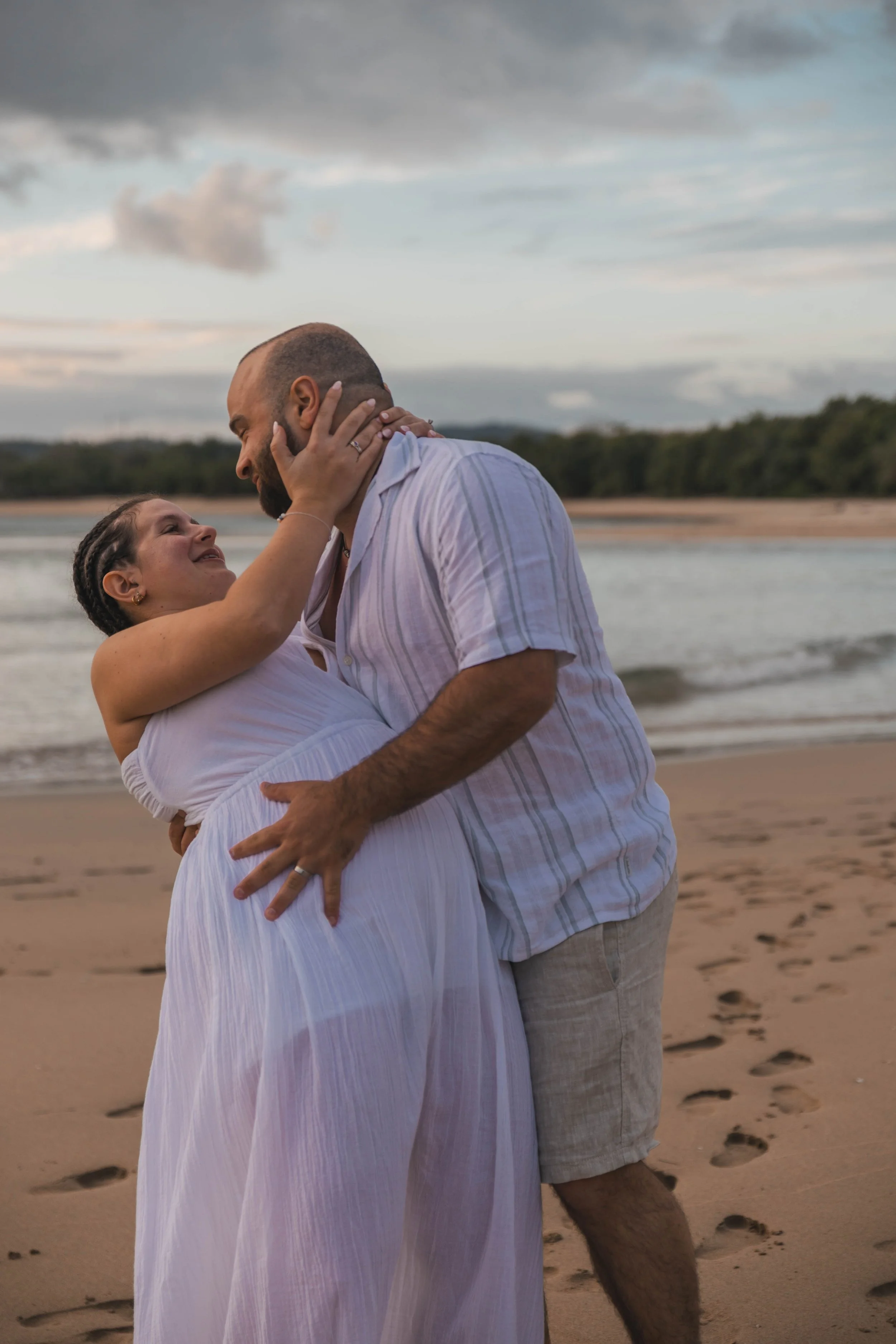 A couple embracing on a beach at sunset, smiling and looking into each other's eyes.