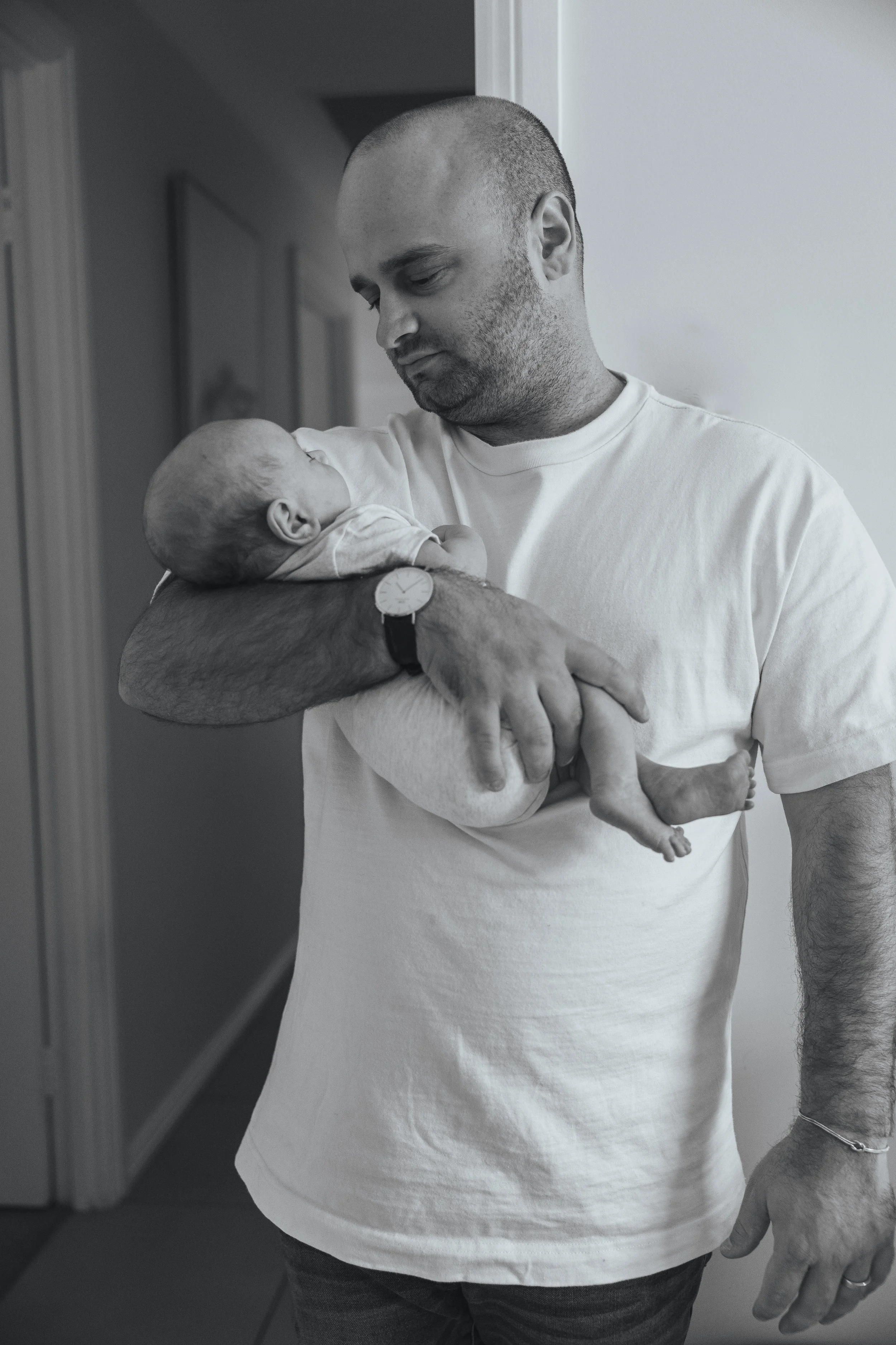 A man holding a newborn baby in his arms, looking at the baby lovingly, in black and white.
