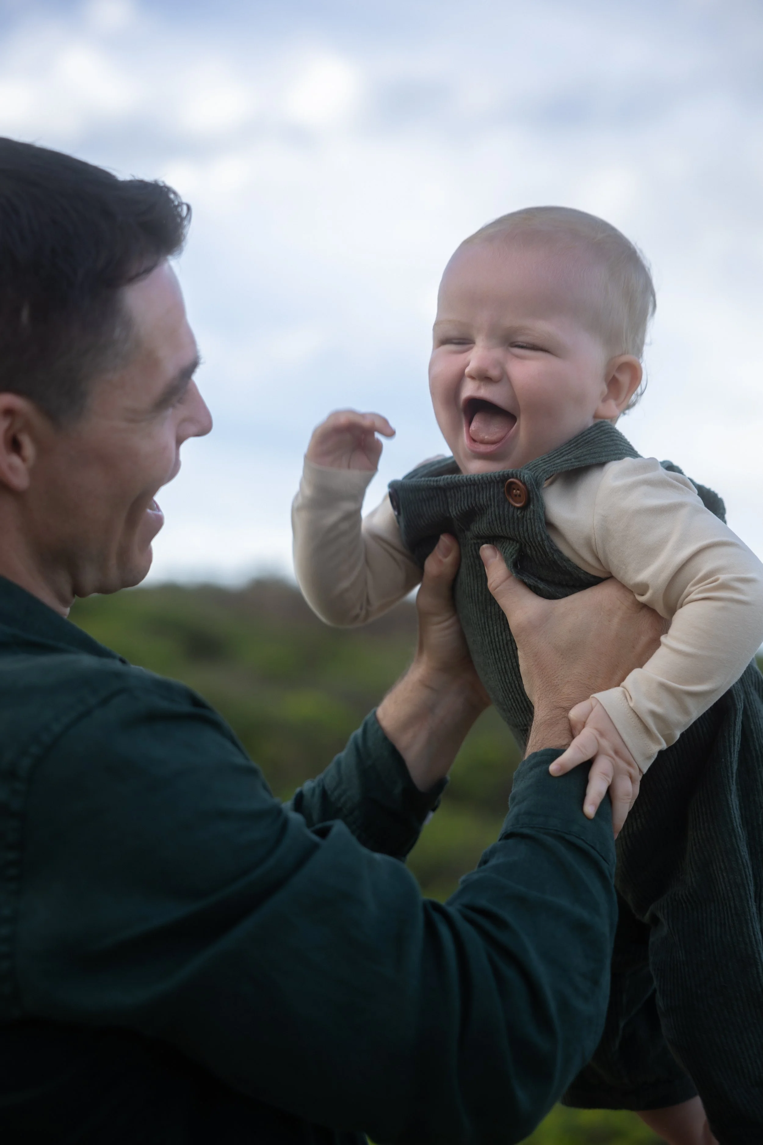 A man holding a laughing baby outdoors against a cloudy sky.