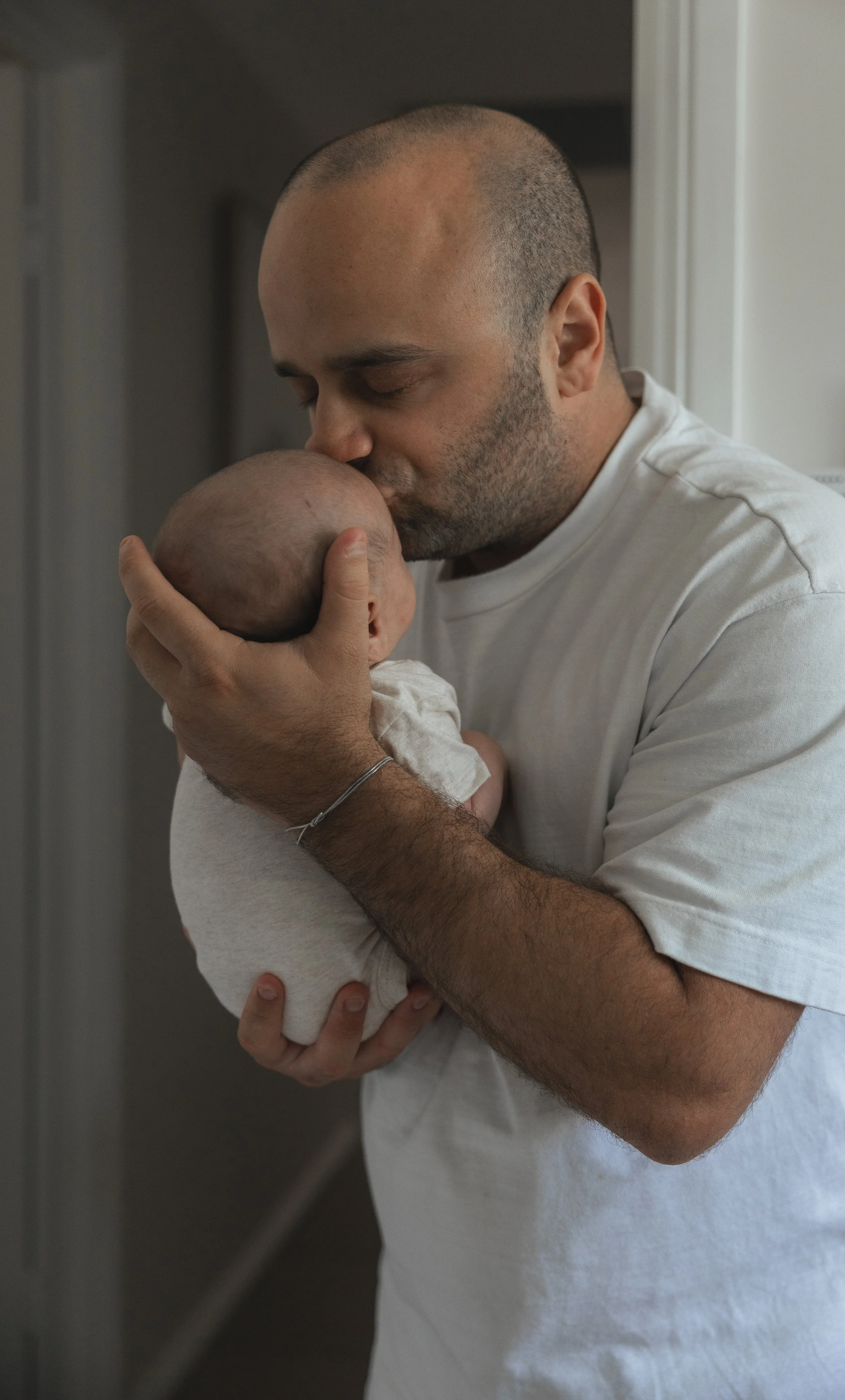 A man kissing a baby's head while holding the baby close to his face. The baby is wearing a light-colored outfit.