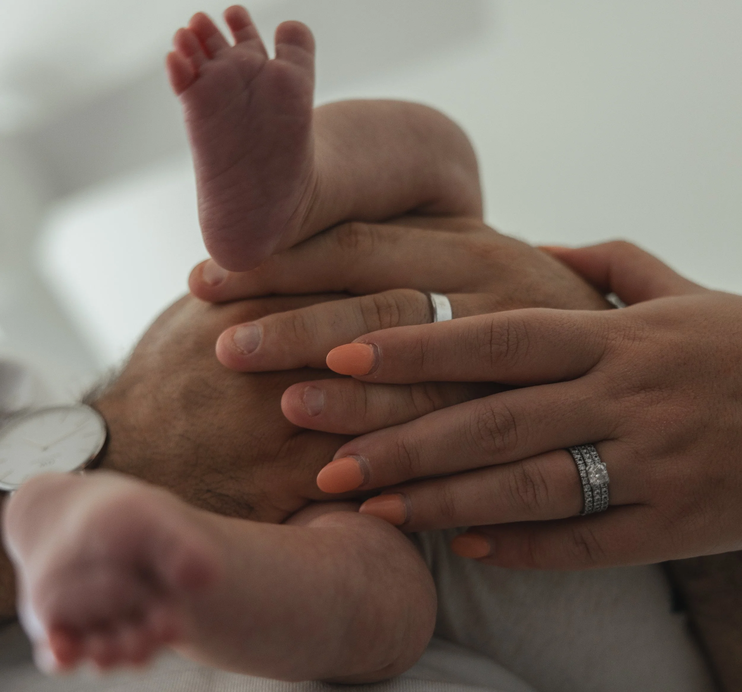 Close-up of a newborn baby lying on an adult's chest, with small hands and feet visible, and the adult's hands gently holding the baby.