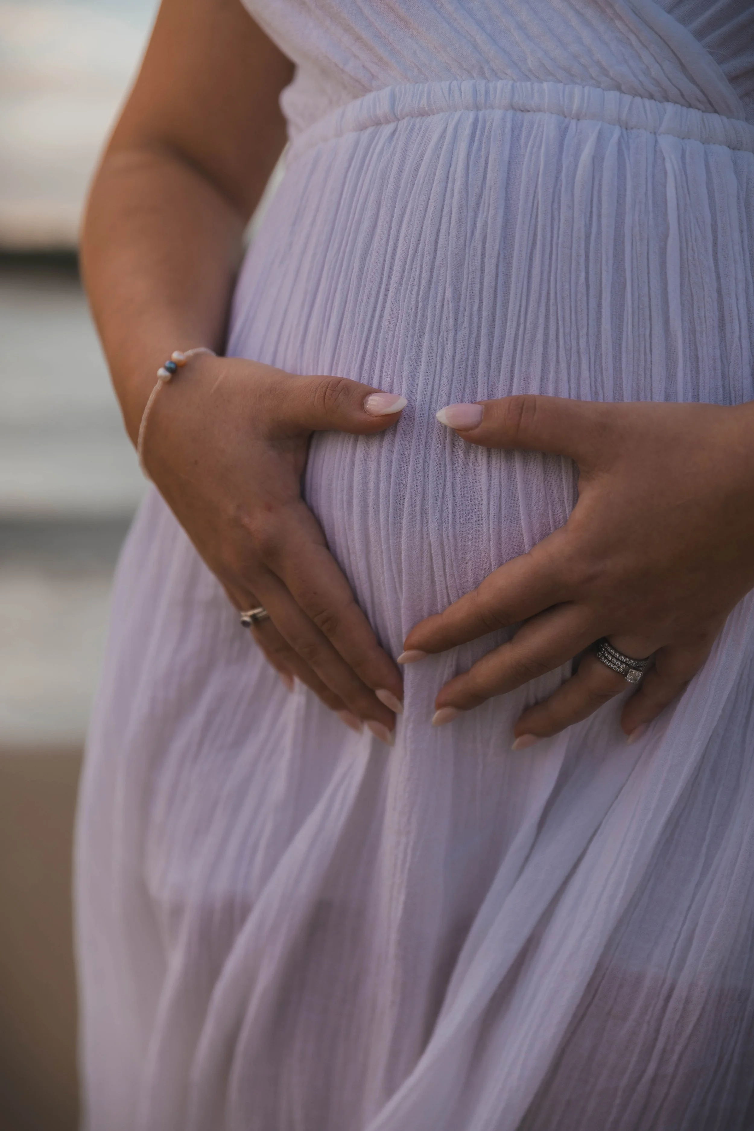 Close-up of pregnant woman's belly with hands gently cradling it, wearing a light, flowing dress.