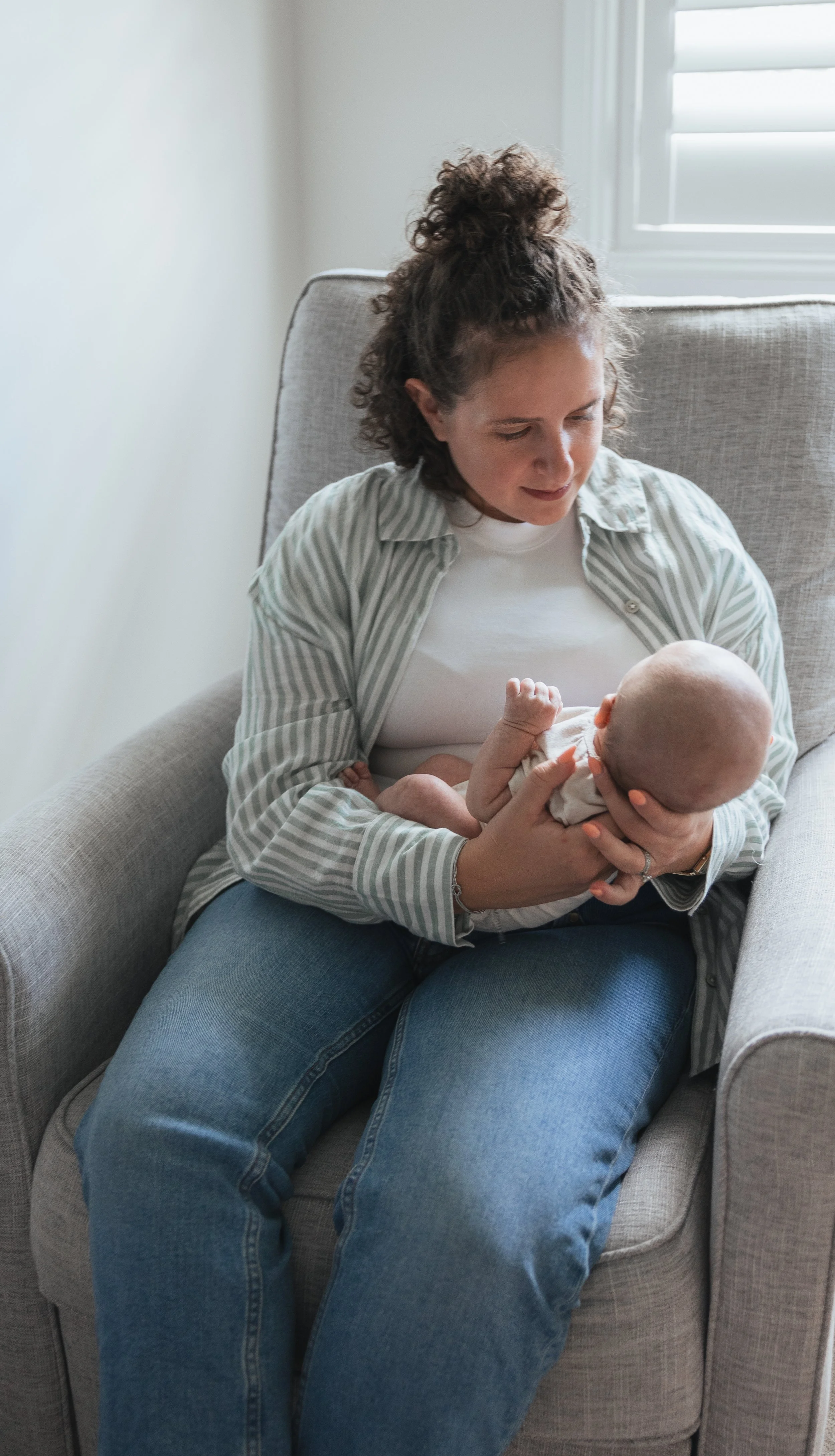 Woman sitting on a beige armchair, holding a bald baby.
