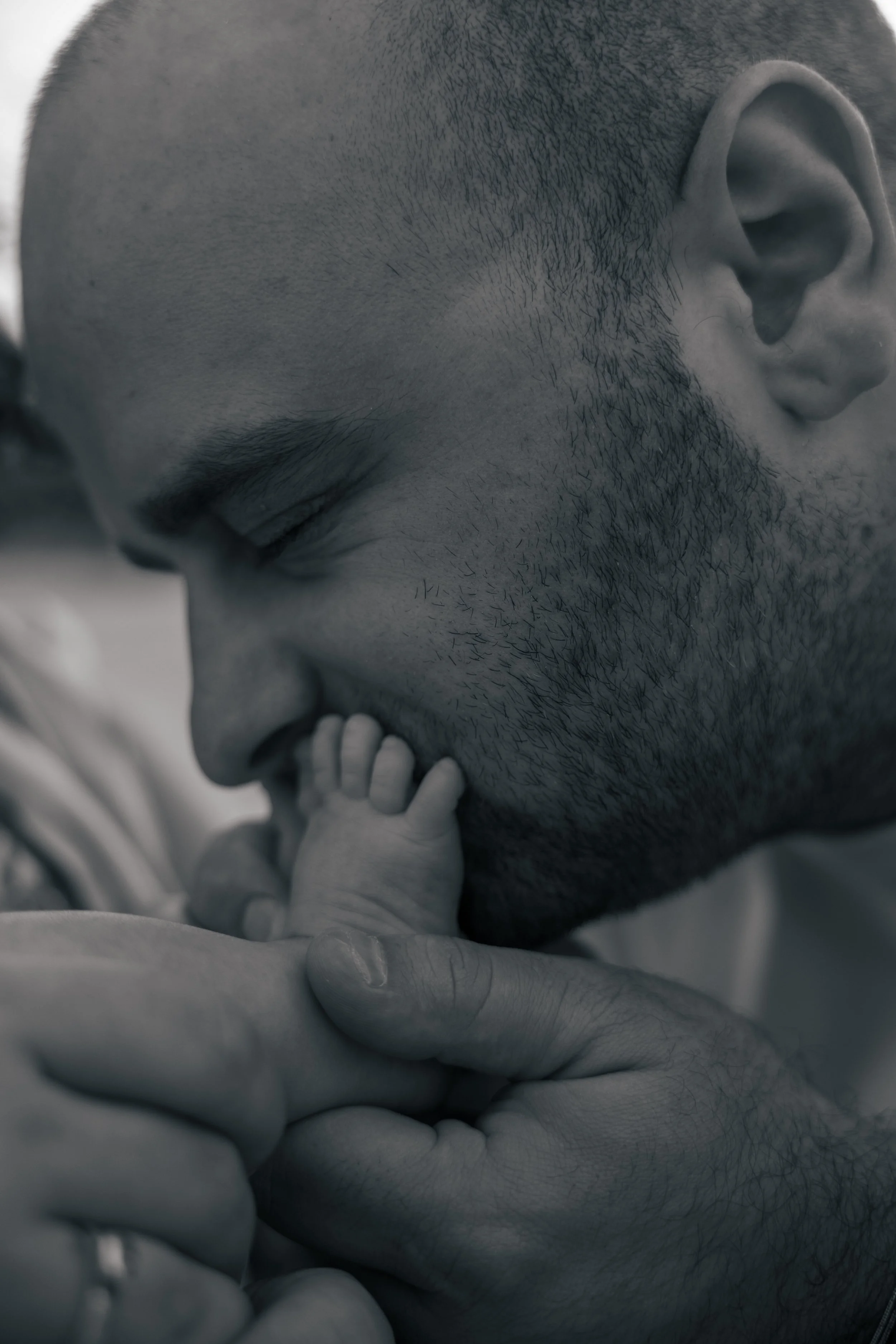 A close-up black-and-white photo of a father kissing his newborn baby on the nose, with the baby holding onto the father's finger.
