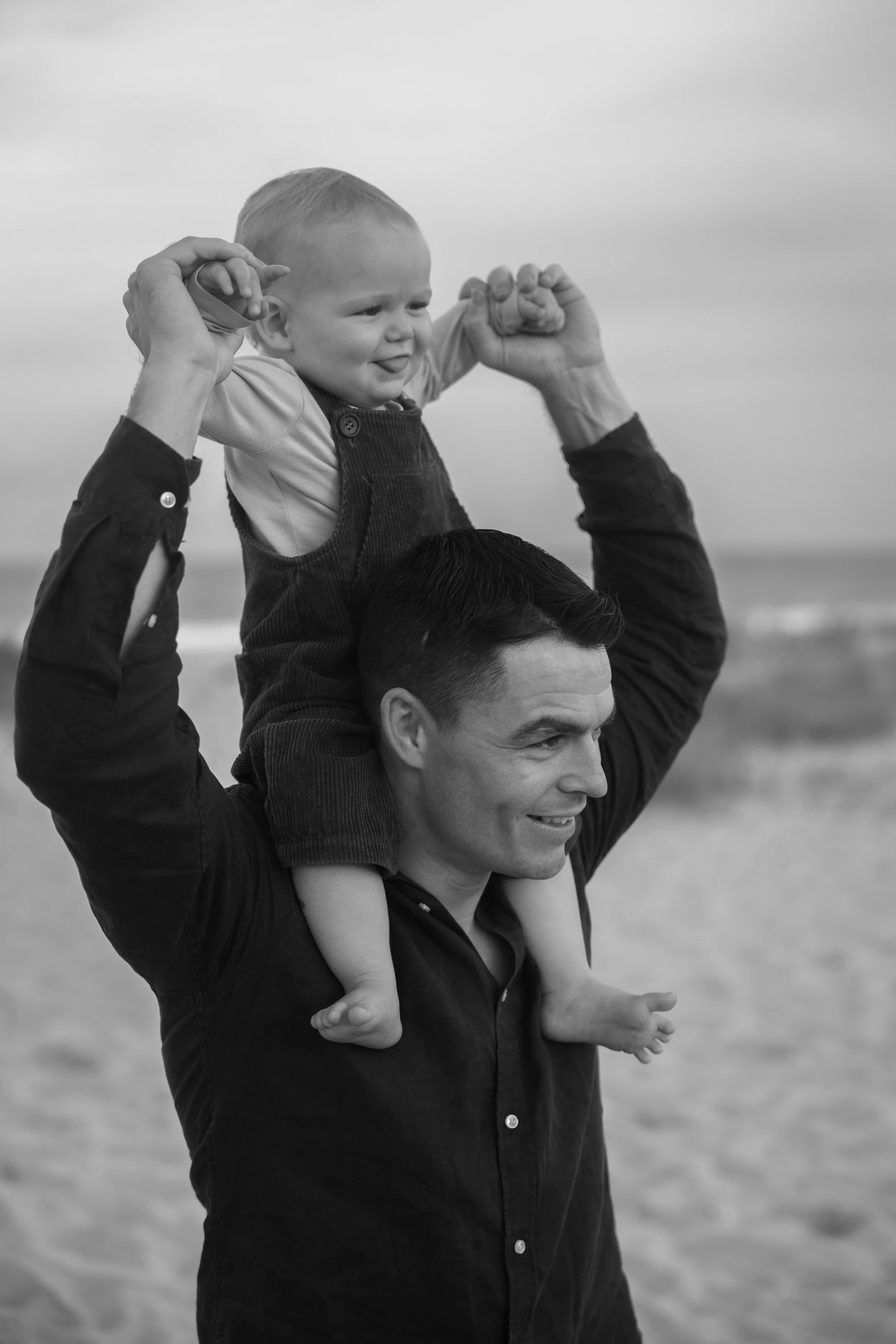 A father carrying his young son on his shoulders at the beach.