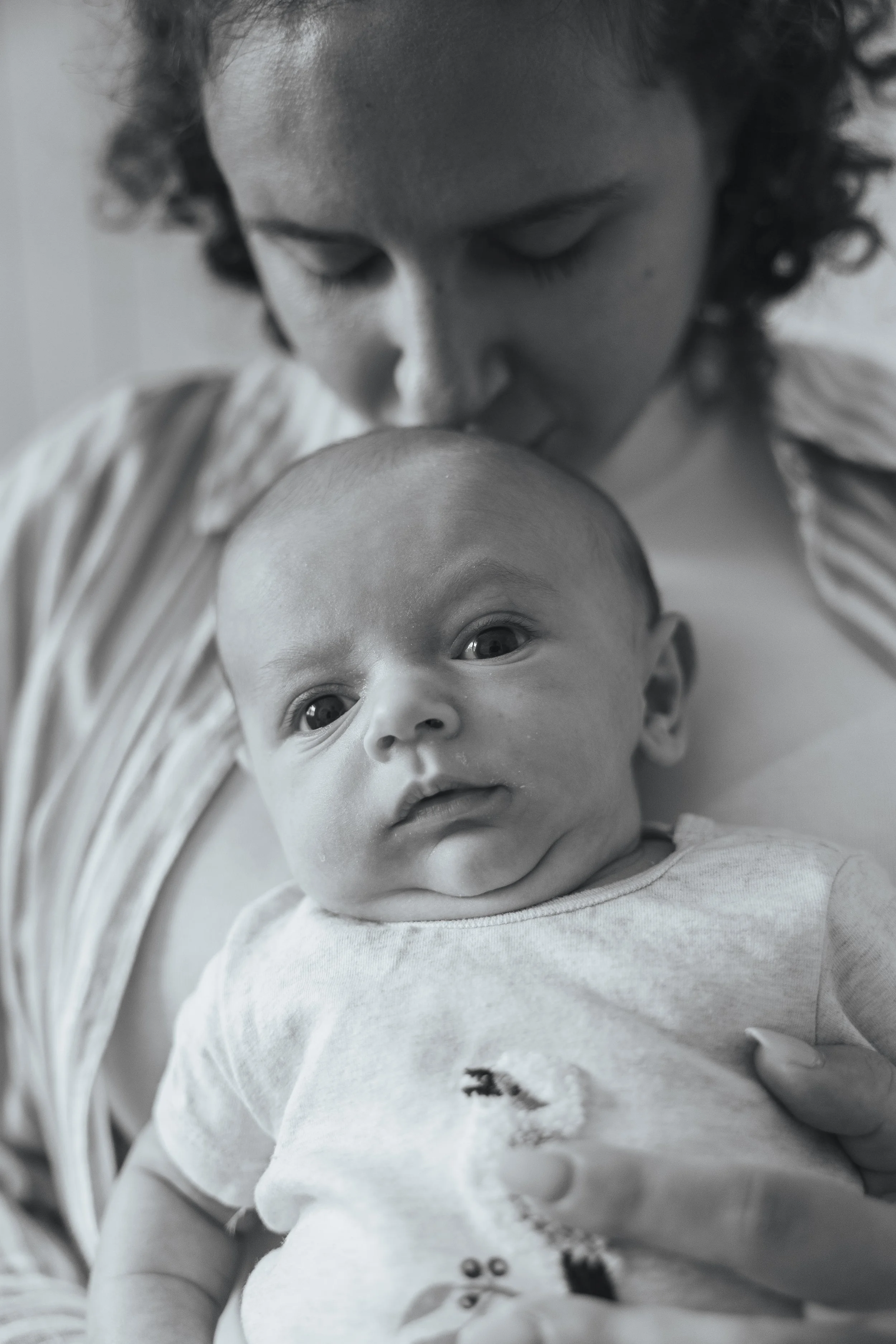 A woman gently kisses a baby's head in a close-up black-and-white photo.