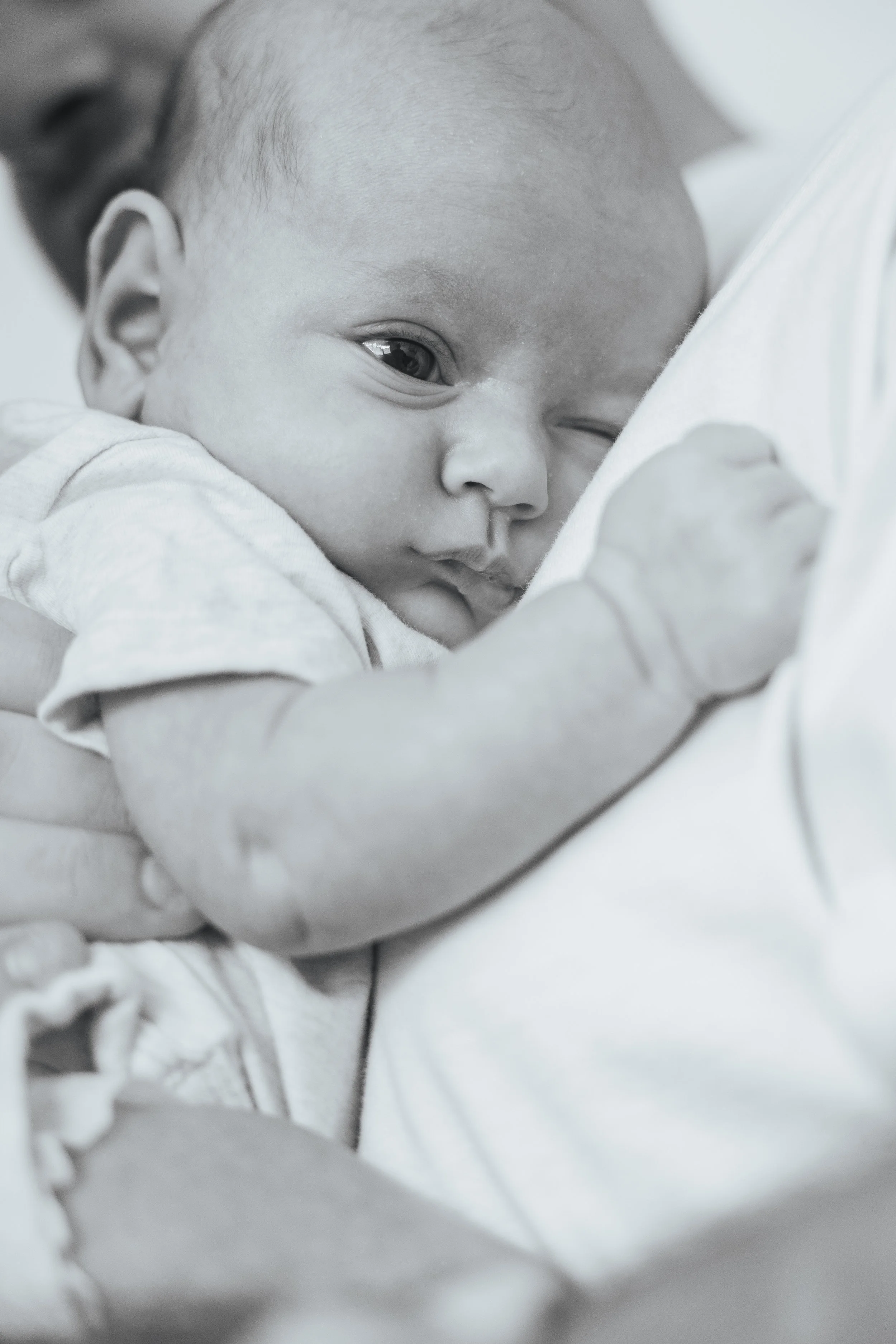 Close-up of a baby resting on someone's shoulder, looking to the side with a calm expression.