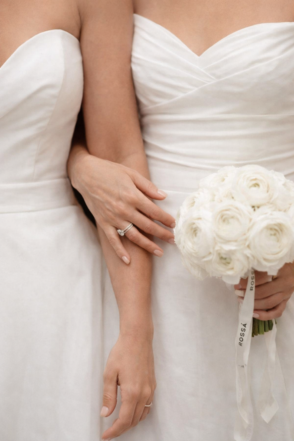 two brides standing together, one hand with a wedding ring holding the other's arm