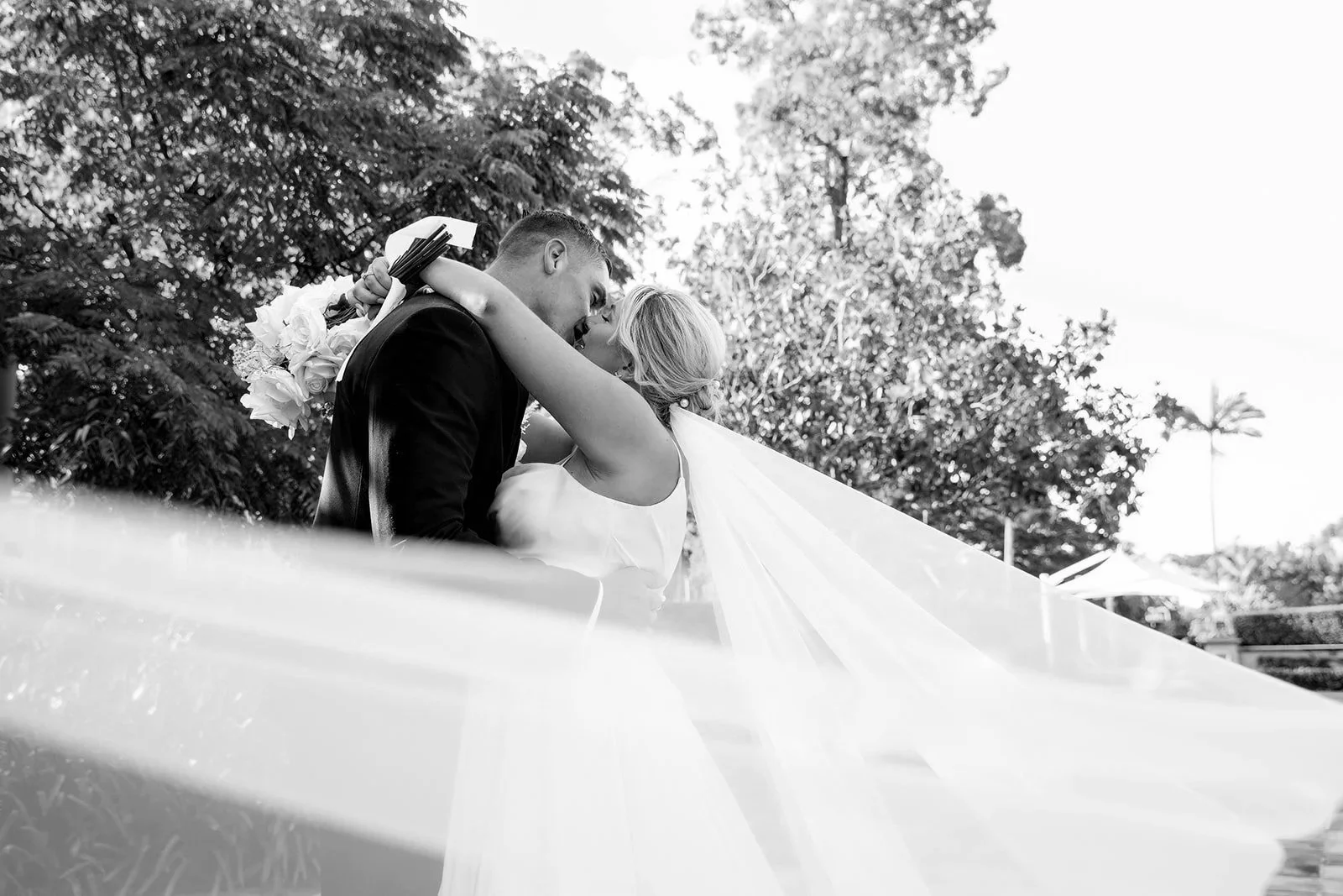 bride and groom kissing with veil flying in the wind
