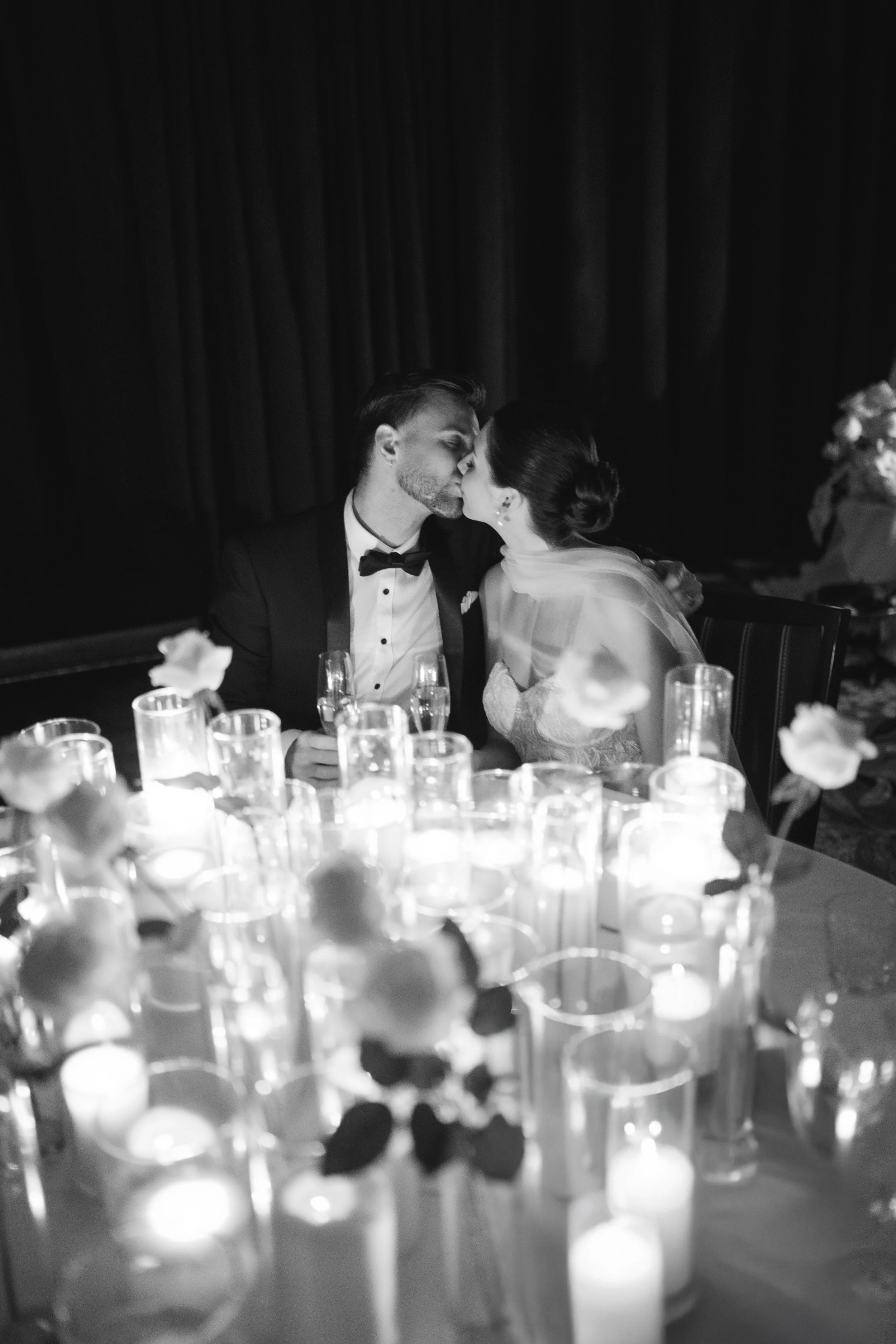 newlyweds kissing behind a table of candles and roses