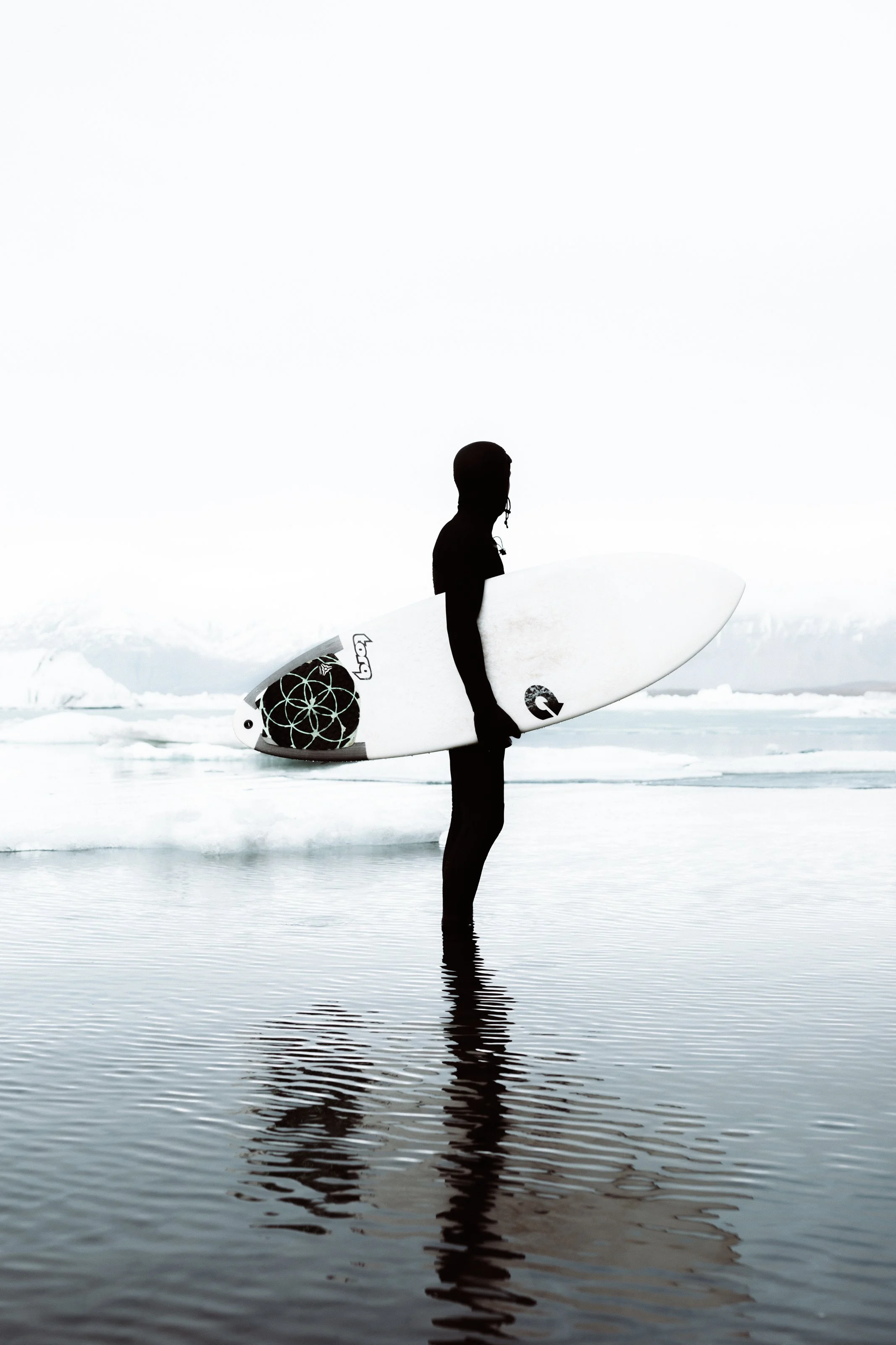 surfer in wetsuit with surfboard looking at ice and snow