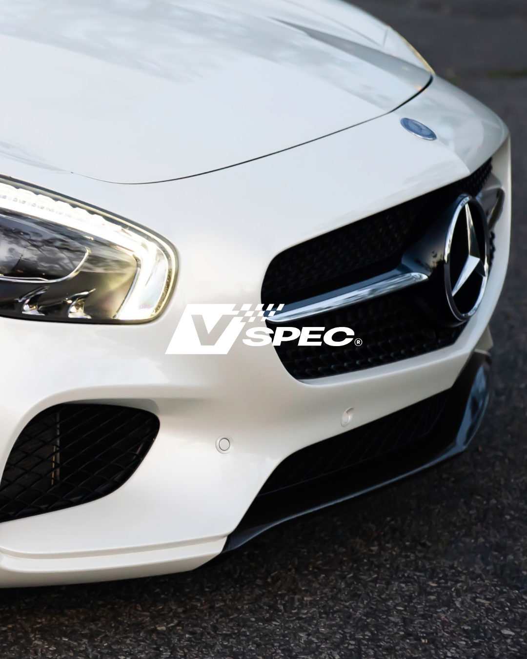 Front view of a white Mercedes-Benz car, focusing on the grille and logo, with "V Spec" text overlay.