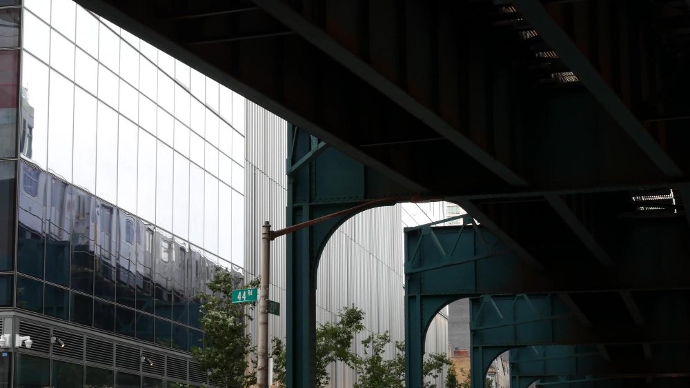 An elevated steel transit structure running alongside a modern glass corporate office building reflecting the city landscape, representing structural security and credibility.
