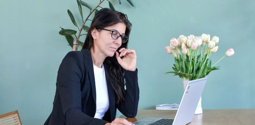 A woman wearing glasses sits at a table, working on a laptop, representing a professional attorney's bio.