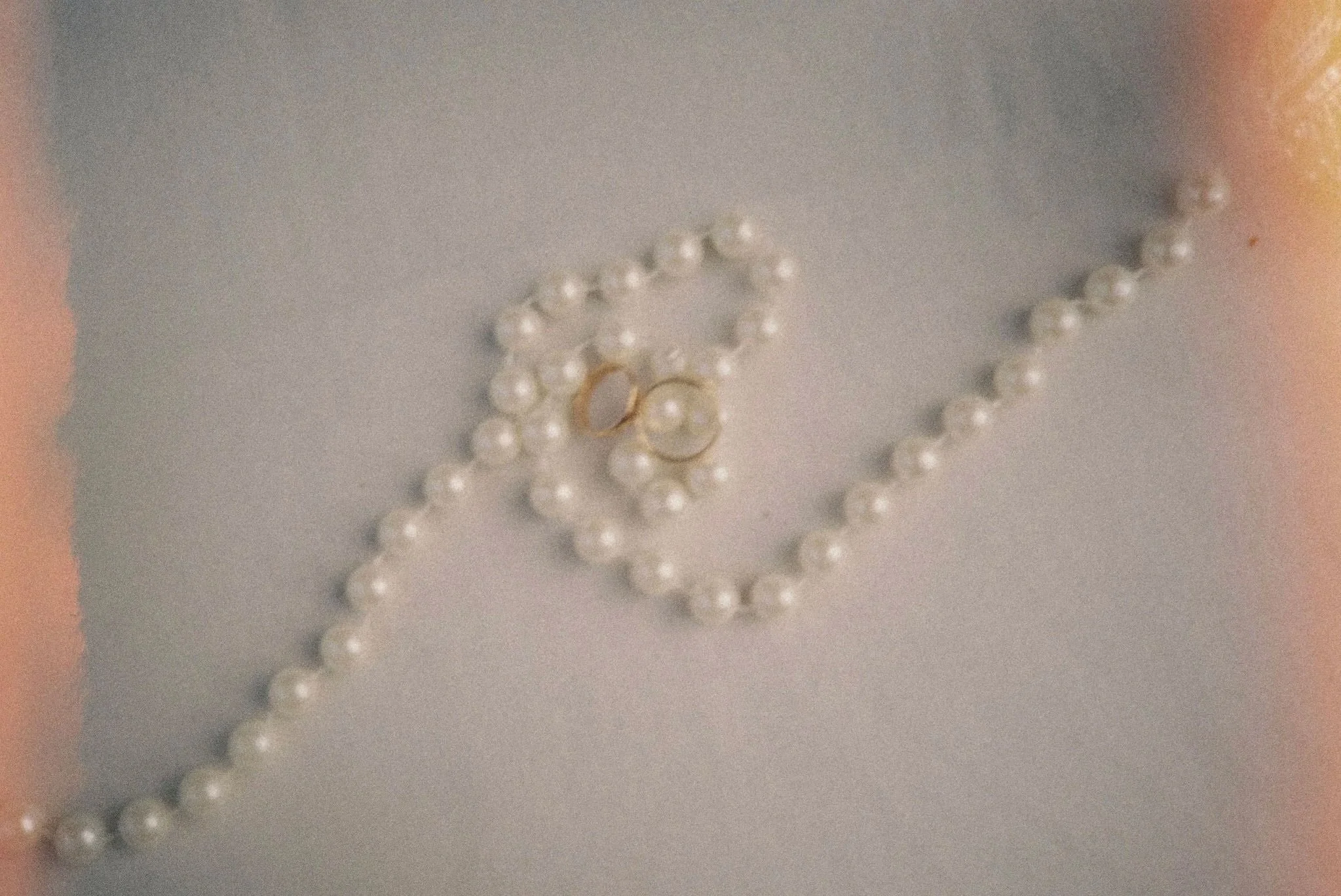 Close-up of pearl jewelry including a pearl necklace, a pearl bracelet, and pearl earrings on a plain surface.