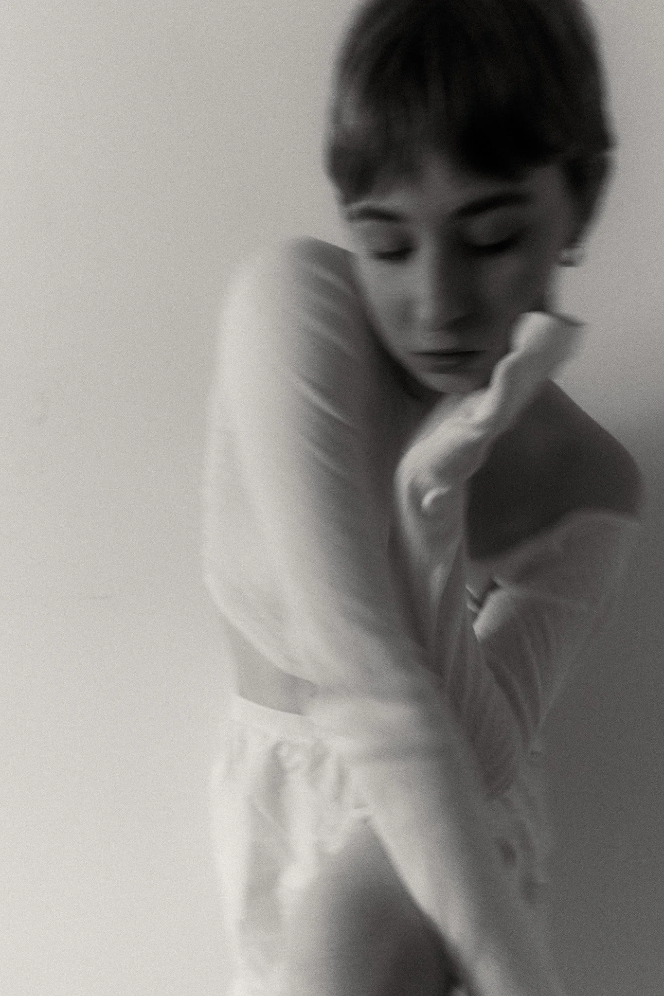 Black and white photo of a woman with short hair, eyes closed, and her hand touching her face, wearing a loose white shirt.