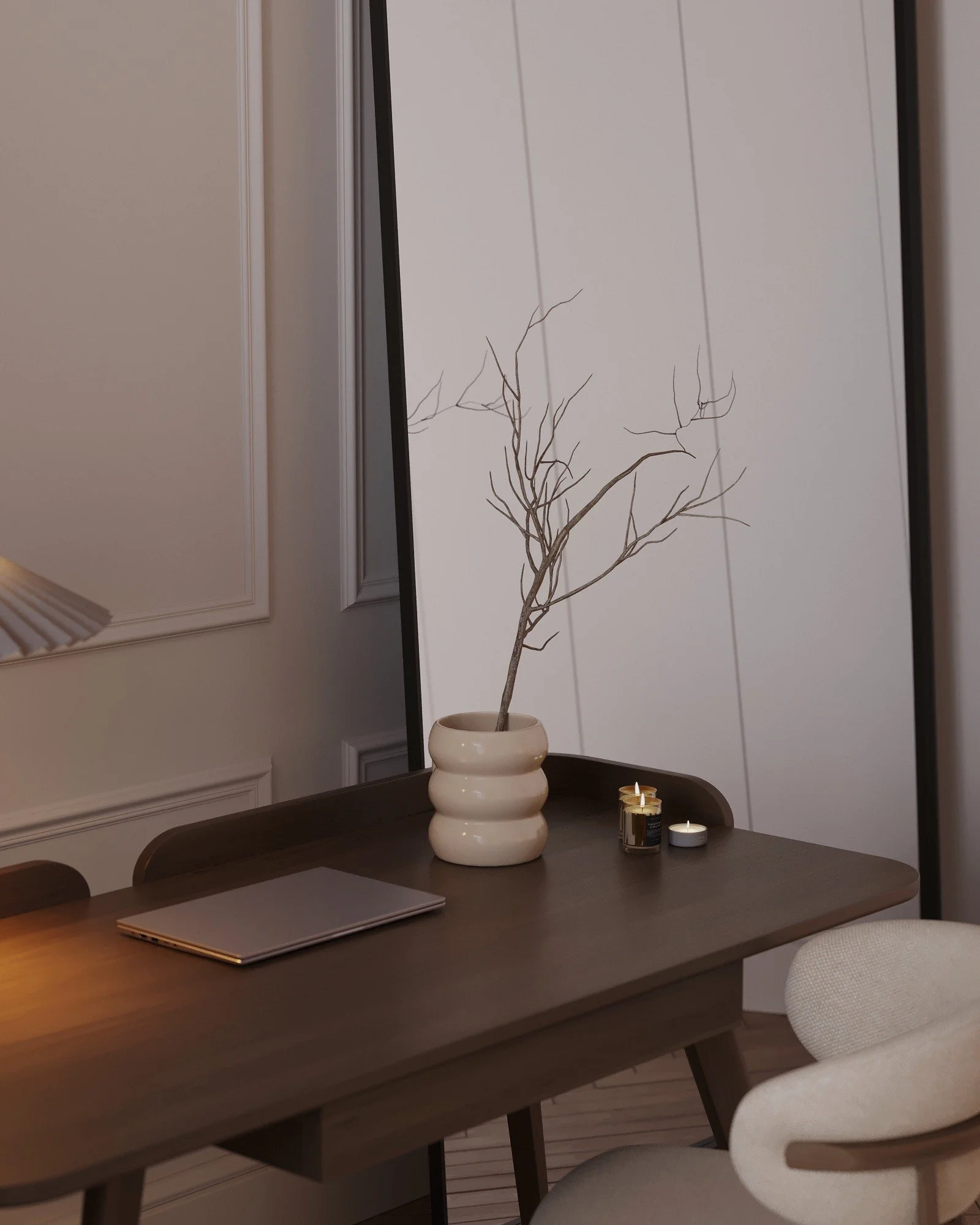 A wooden dining table with a closed laptop, a white decorative vase with a leafless branch, and three small candles in black and white holders. A mirror behind reflects the wall with white paneling.