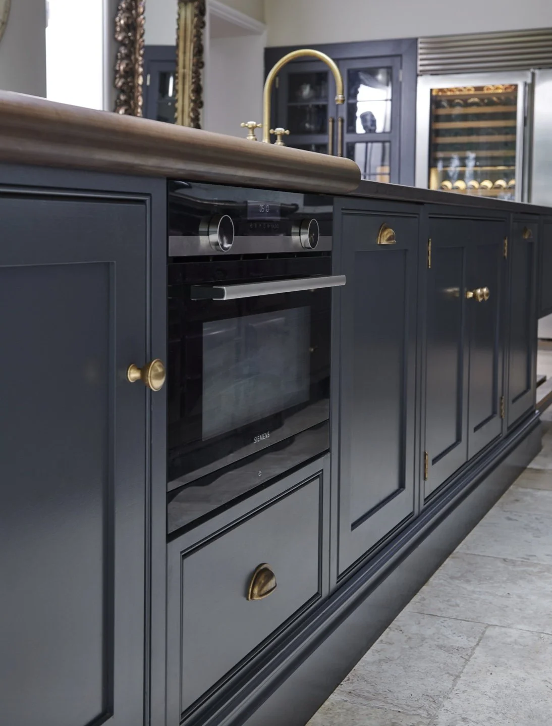 Kitchen island with dark cabinets, gold handle pulls, stainless steel oven, and gold faucet over a wooden countertop.
