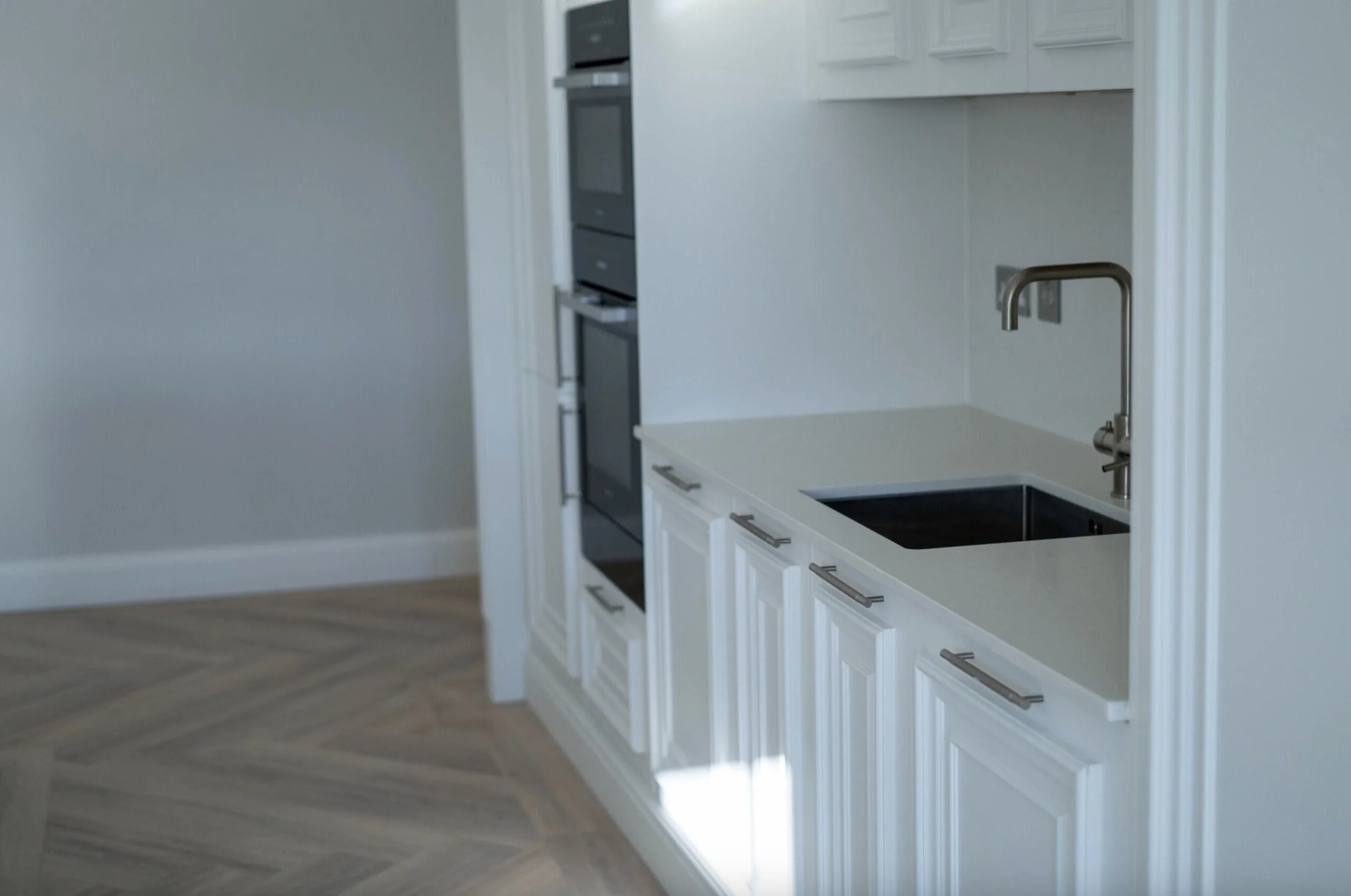 Modern kitchen with white cabinets, black sink, stainless steel faucet, appliances, and wooden floor.