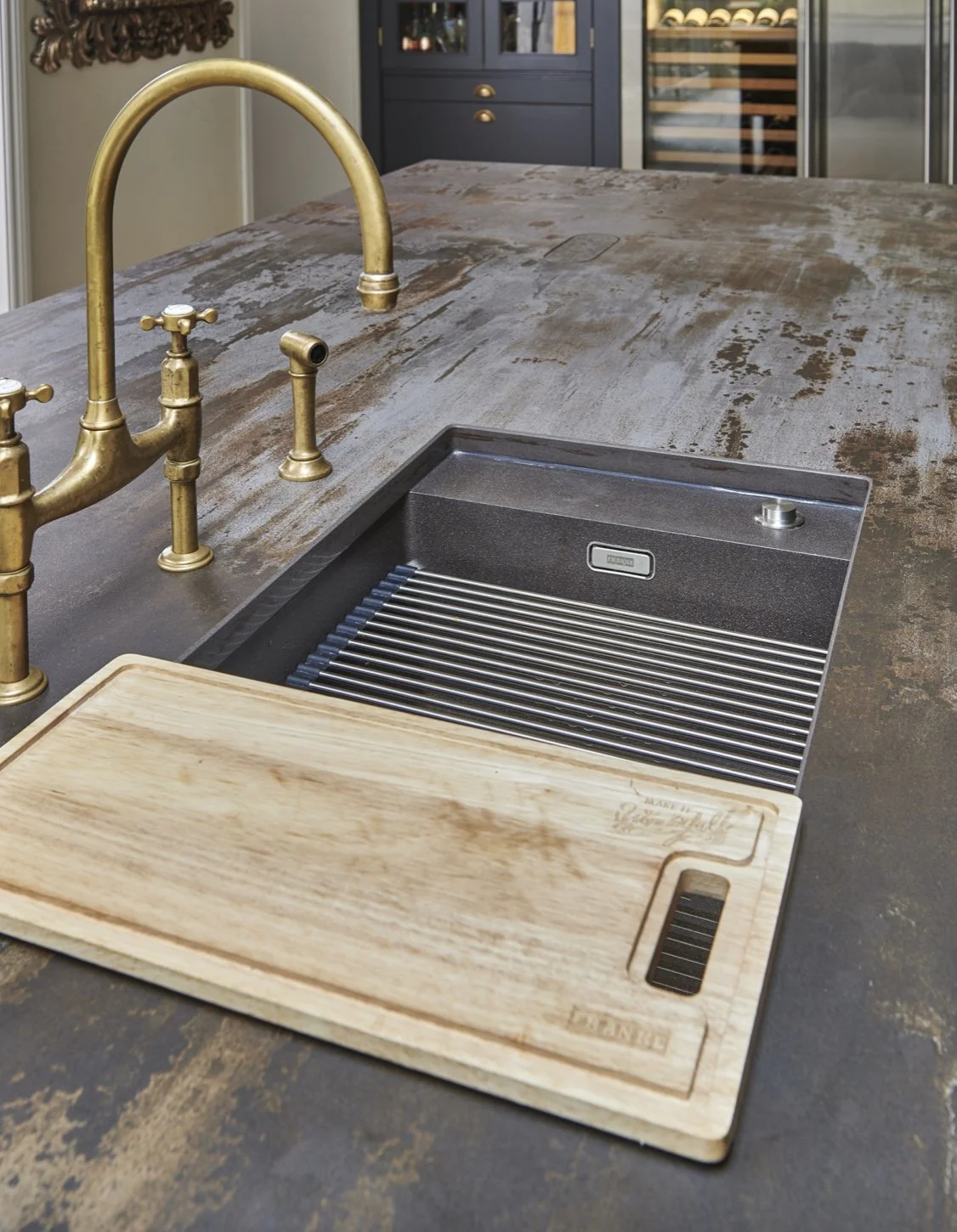 A kitchen island with a rustic wood countertop, a gold faucet, a black kitchen sink with a metal drying rack, and a wooden cutting board.