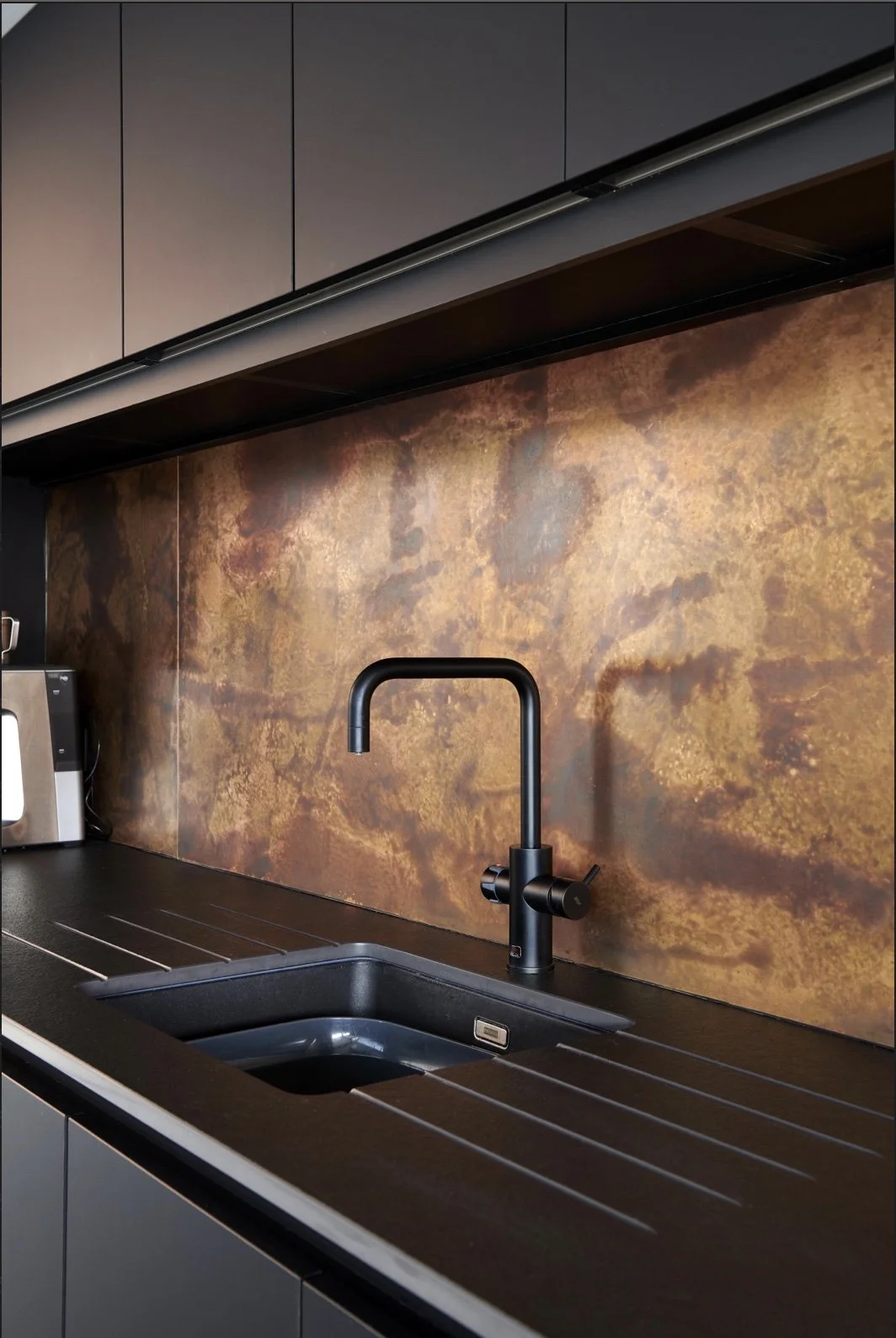 Kitchen sink with a black faucet and a brown textured backsplash wall.