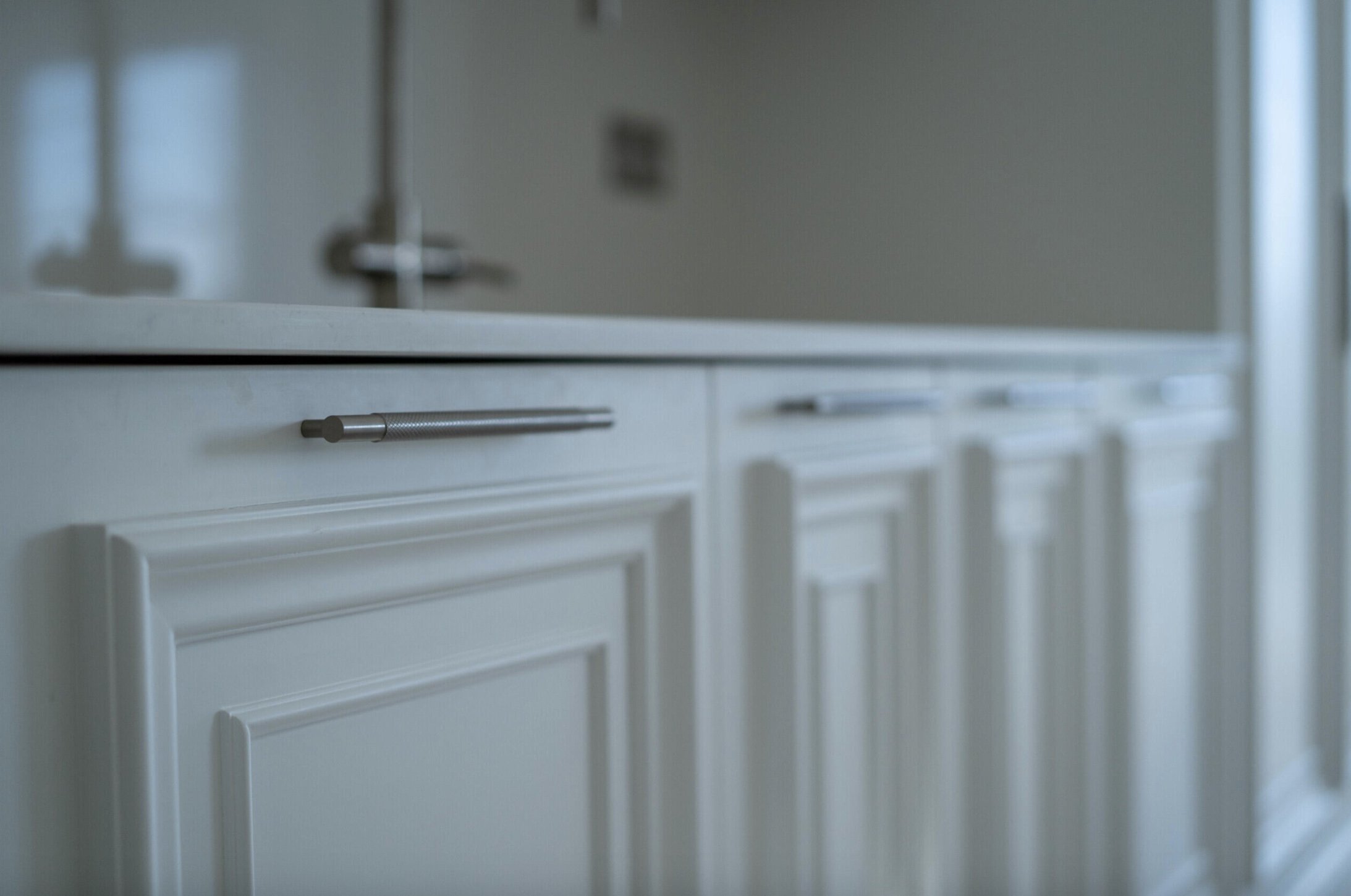 Close-up of white kitchen cabinets with silver handles, blurred in the background.