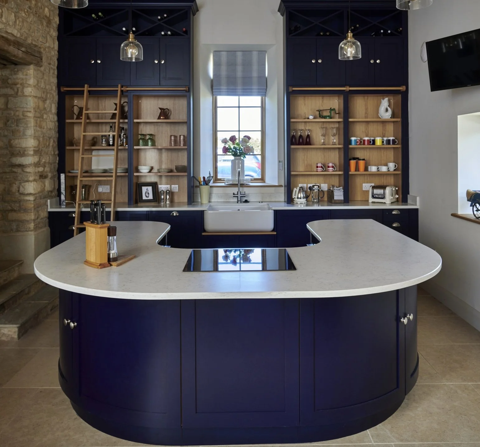 Kitchen with navy blue cabinetry, open wooden shelves, a large window with flower vase, and an island with a built-in stovetop.