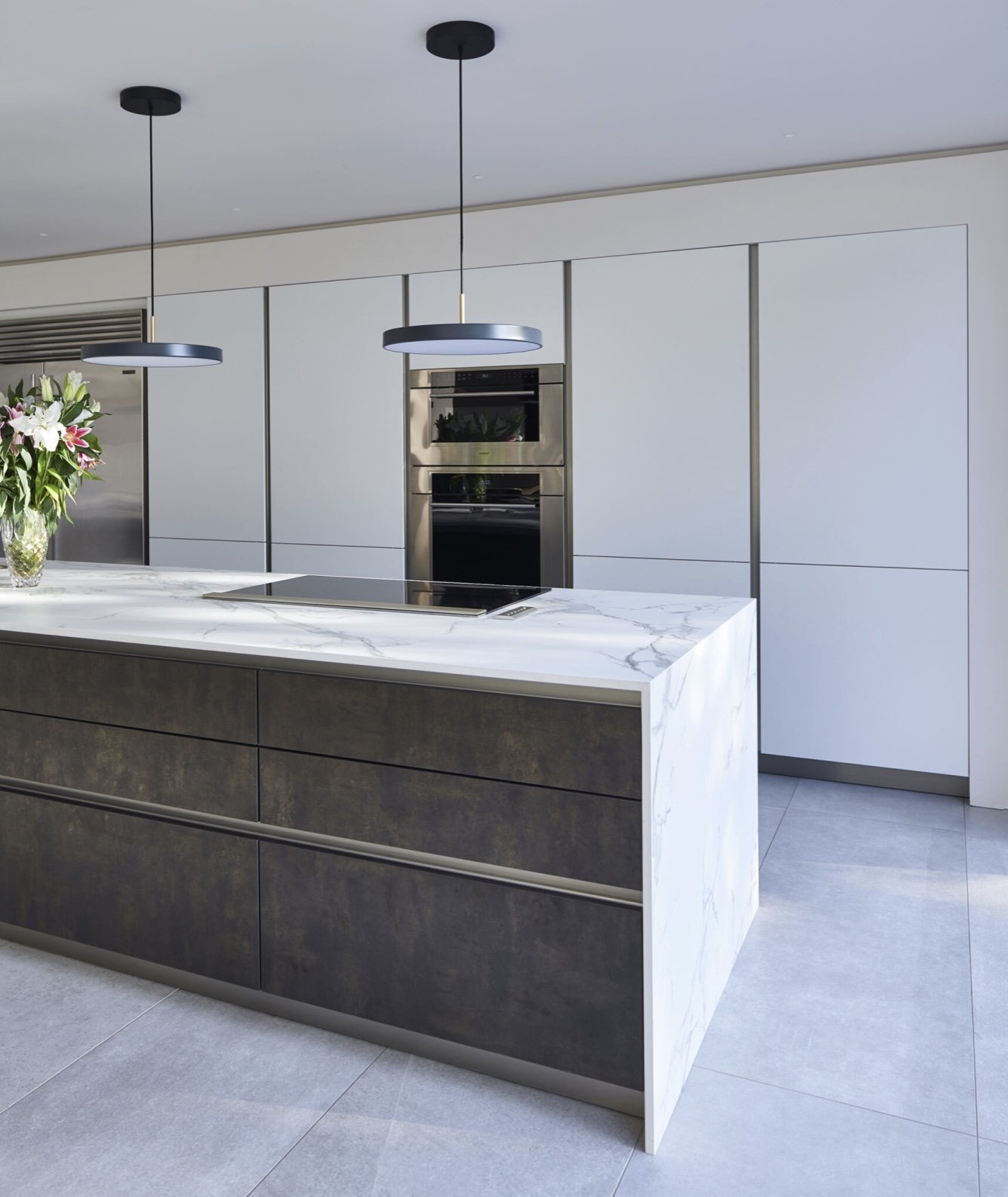 Modern kitchen with white cabinets, marble island, black pendant lights, and stainless steel appliances.
