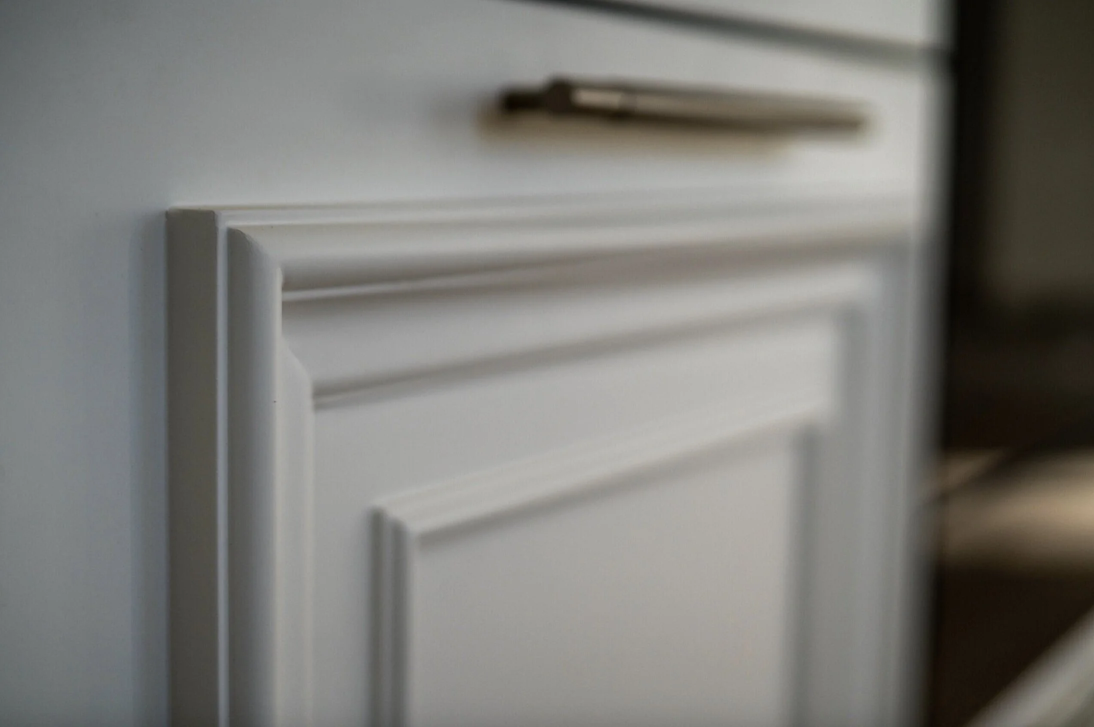 Close-up of white kitchen cabinet with a blurred object on top.