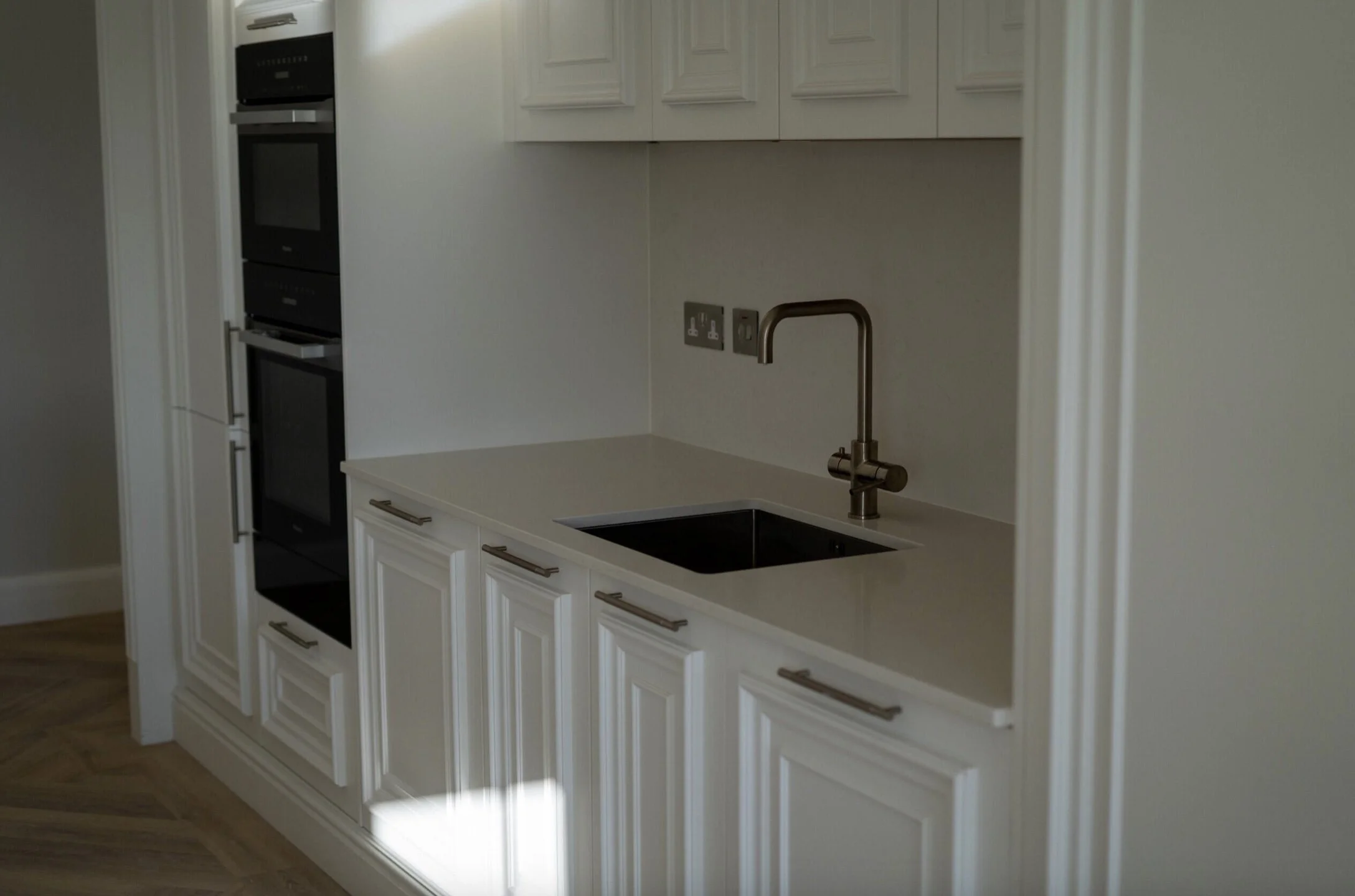 Modern kitchen with white cabinetry, a built-in oven, and a stainless steel faucet over a black sink.