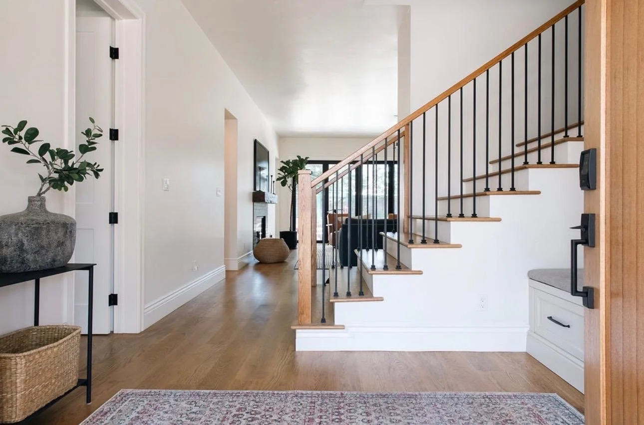 Modern home entry with staircase, hardwood floors, potted plants, and a view into the living room.