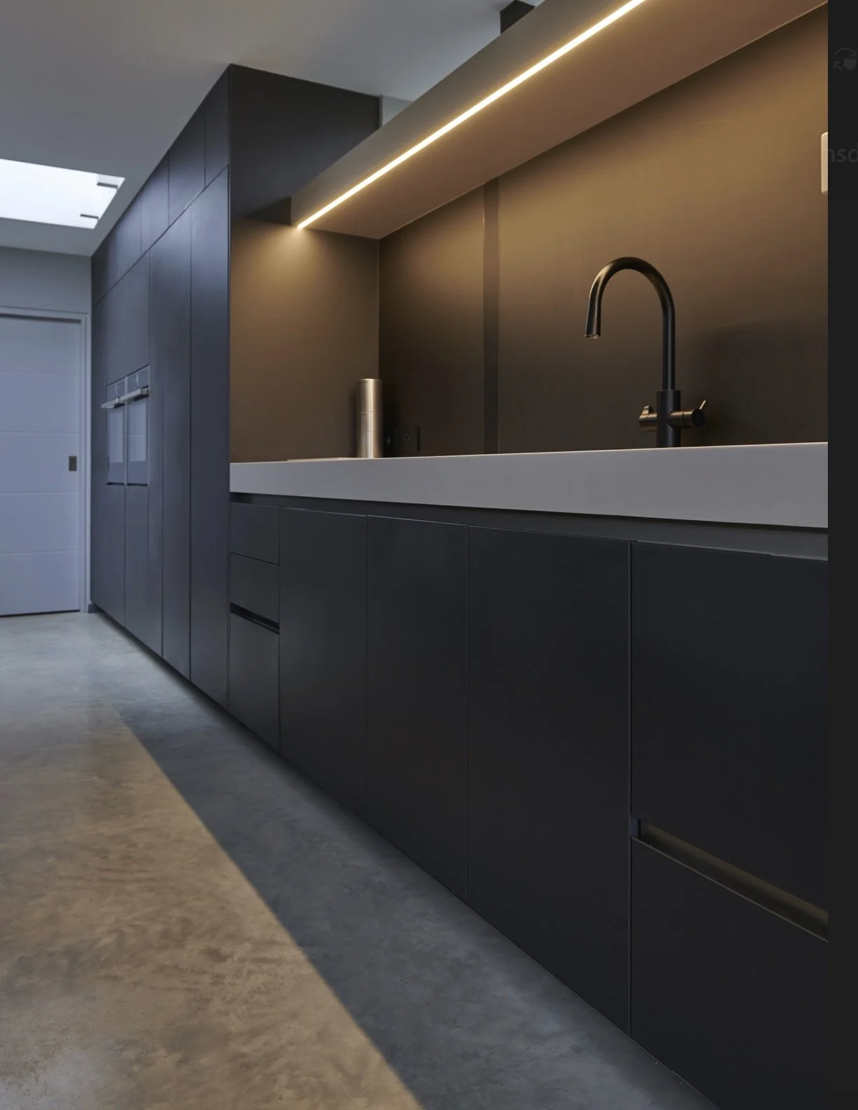 Modern kitchen with dark cabinetry, a white countertop, black faucet, and recessed lighting.