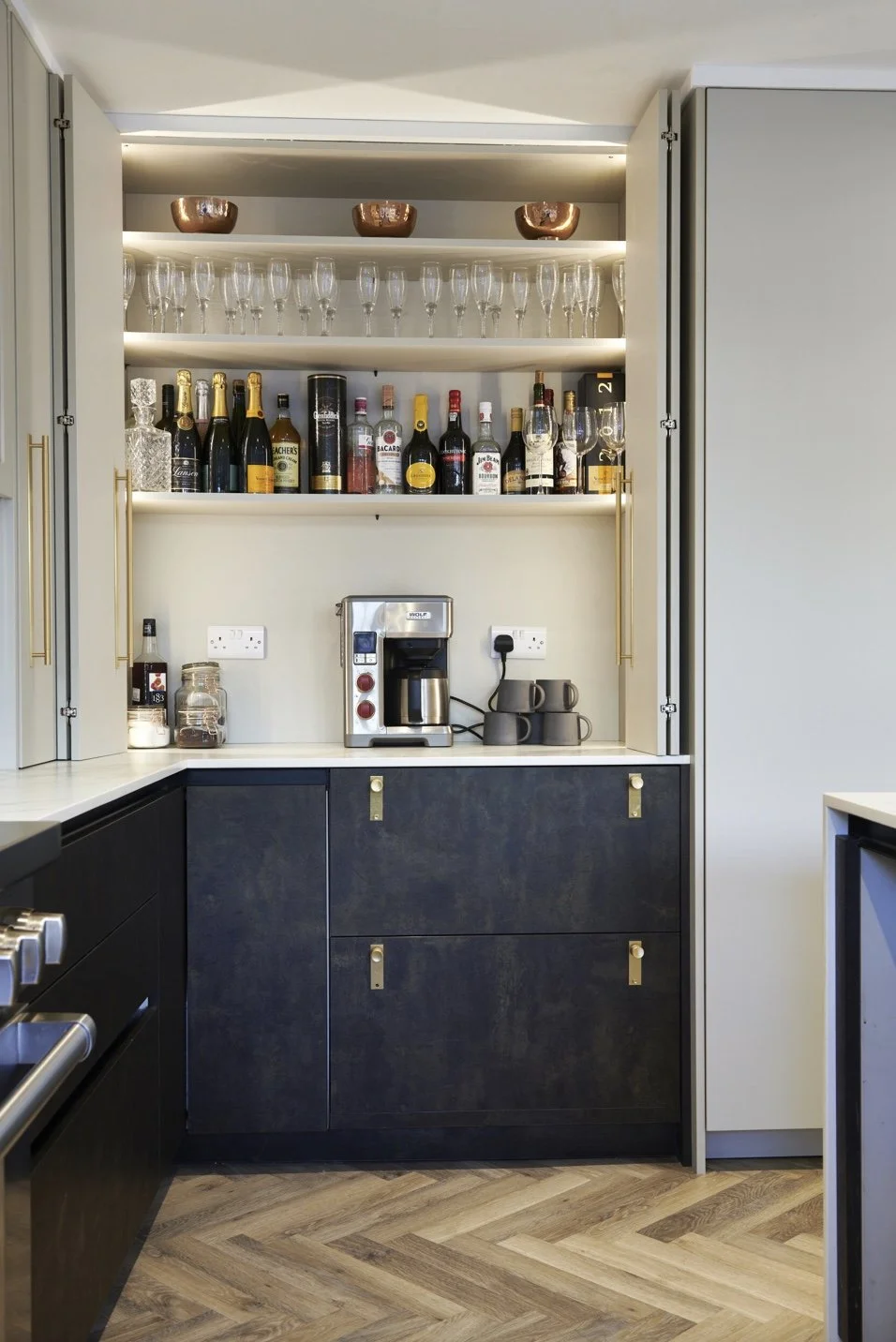 Kitchen cabinet with shelves holding glasses, liquor bottles, and a coffee machine.