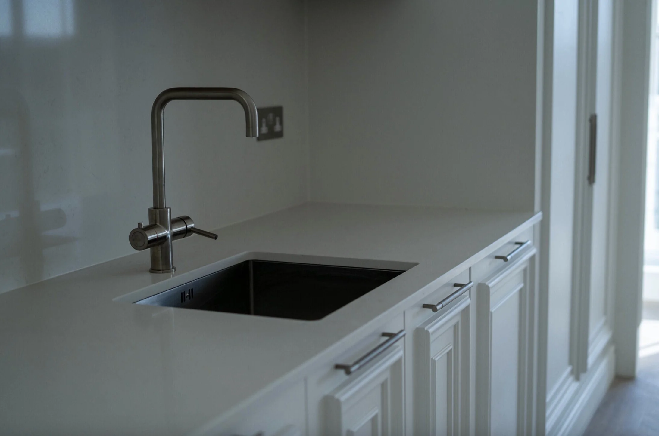 Modern kitchen with a stainless steel faucet and an integrated sink, white cabinets, and a light-colored countertop, next to a sliding glass door.