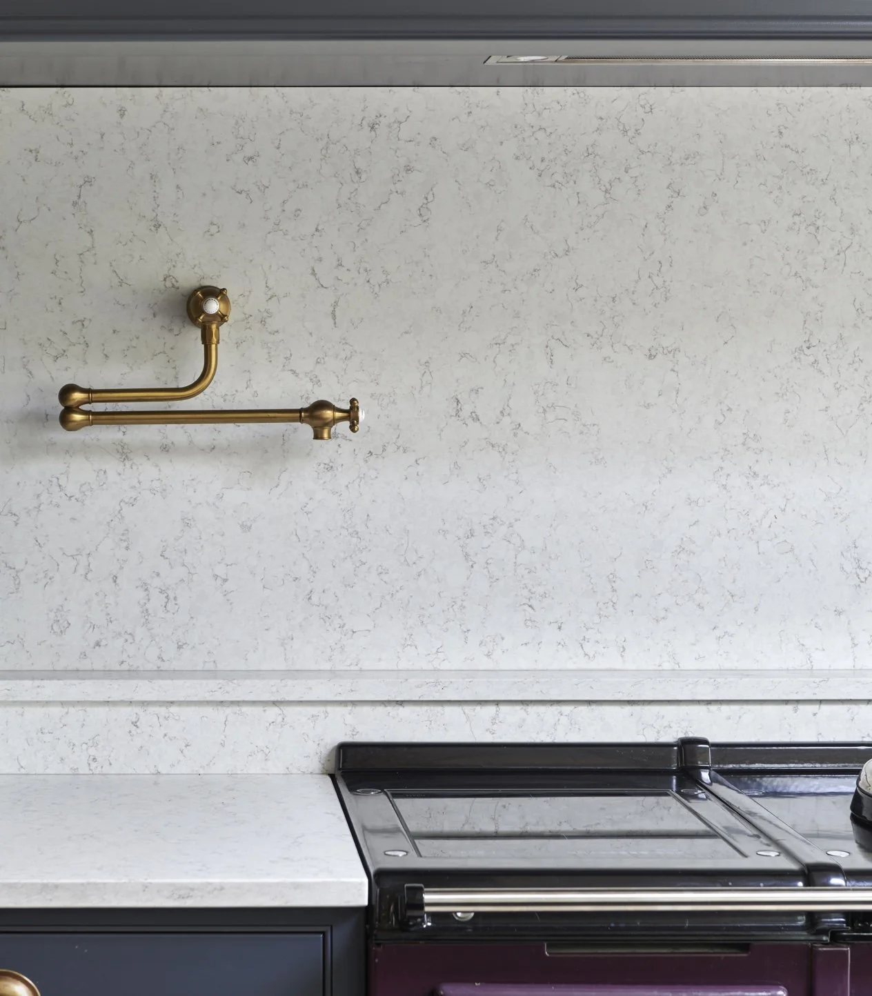 Part of a kitchen with a white speckled countertop, black stove, and a gold-colored faucet on a plain white wall.